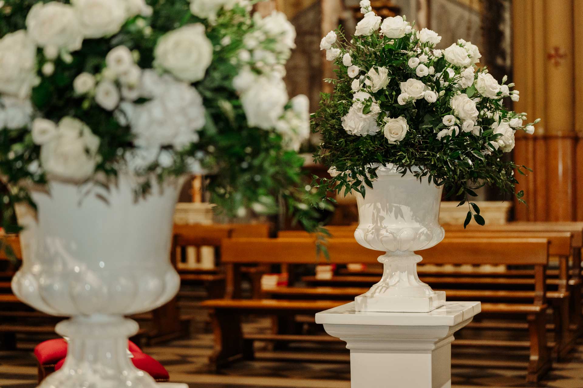 I vasi di fiori bianchi tra le panche della chiesa