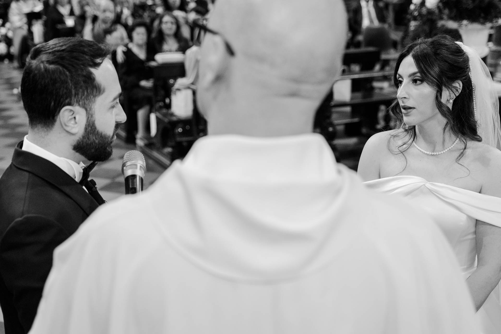 In bianco e nero, la sposa guarda lo sposo oltre la spalla del celebrante