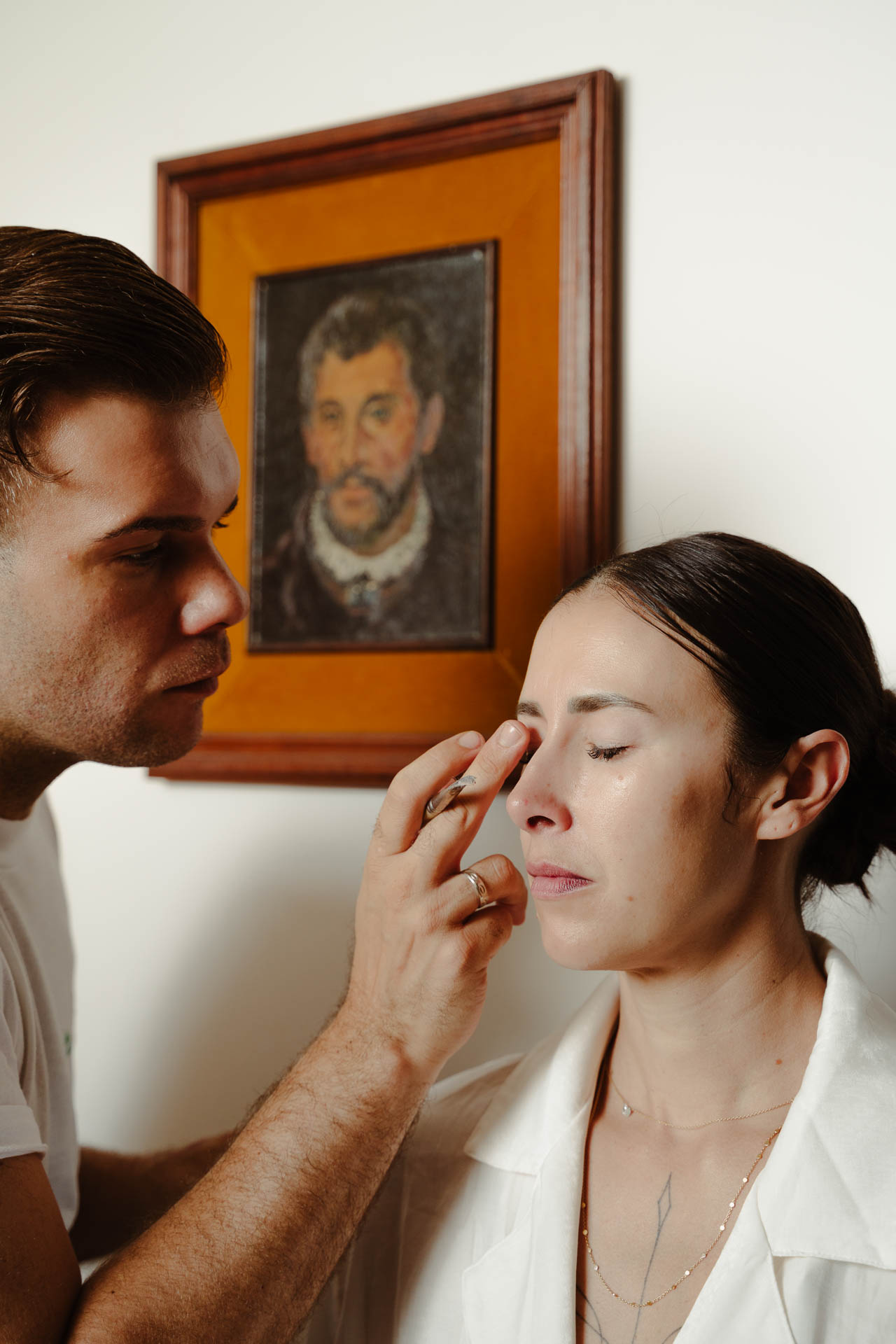 Il truccatore ritocca il viso della sposa, sotto un ritratto antico
