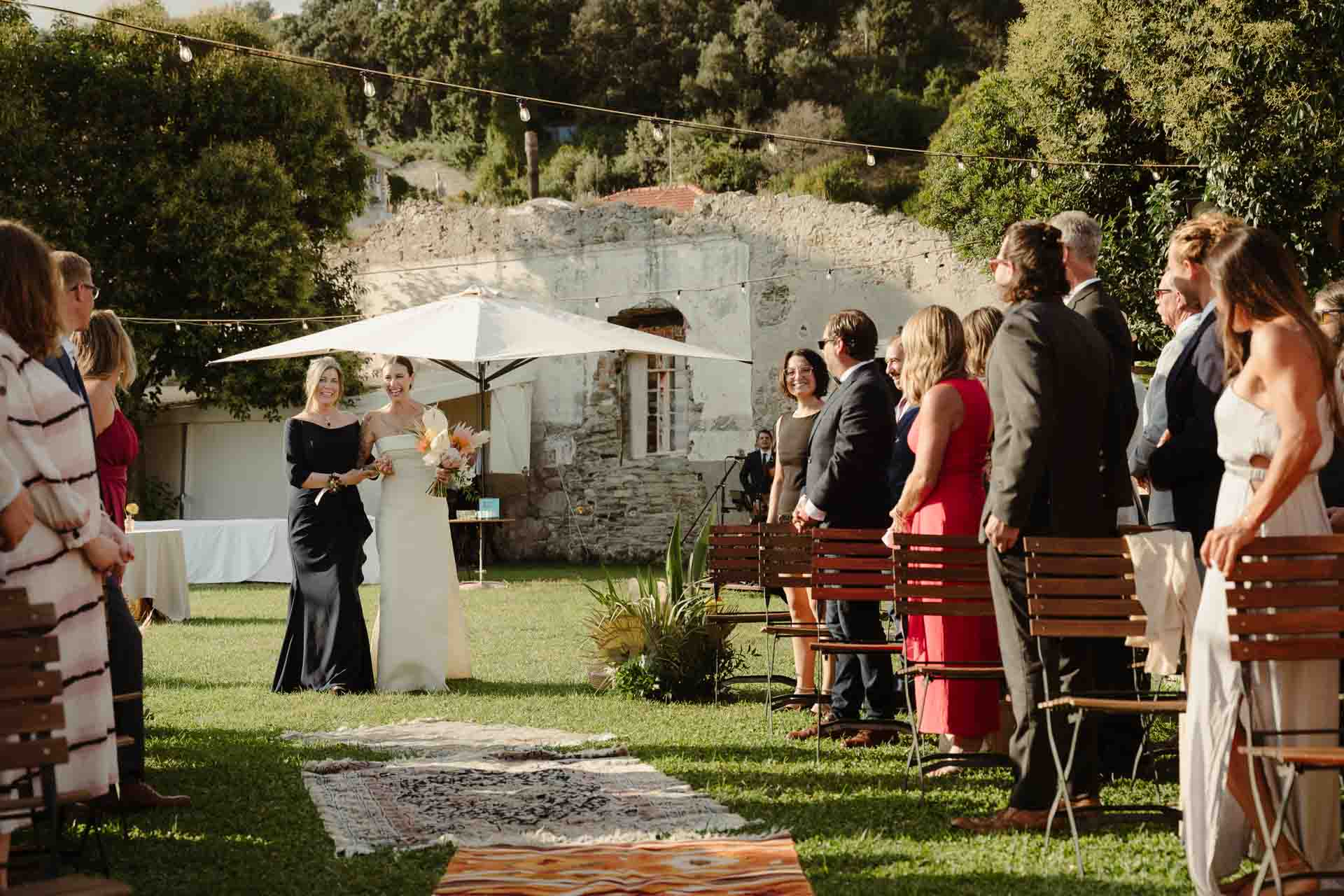 La sposa arriva lungo la navata di tappeti, accompagnata da una signora in abito nero