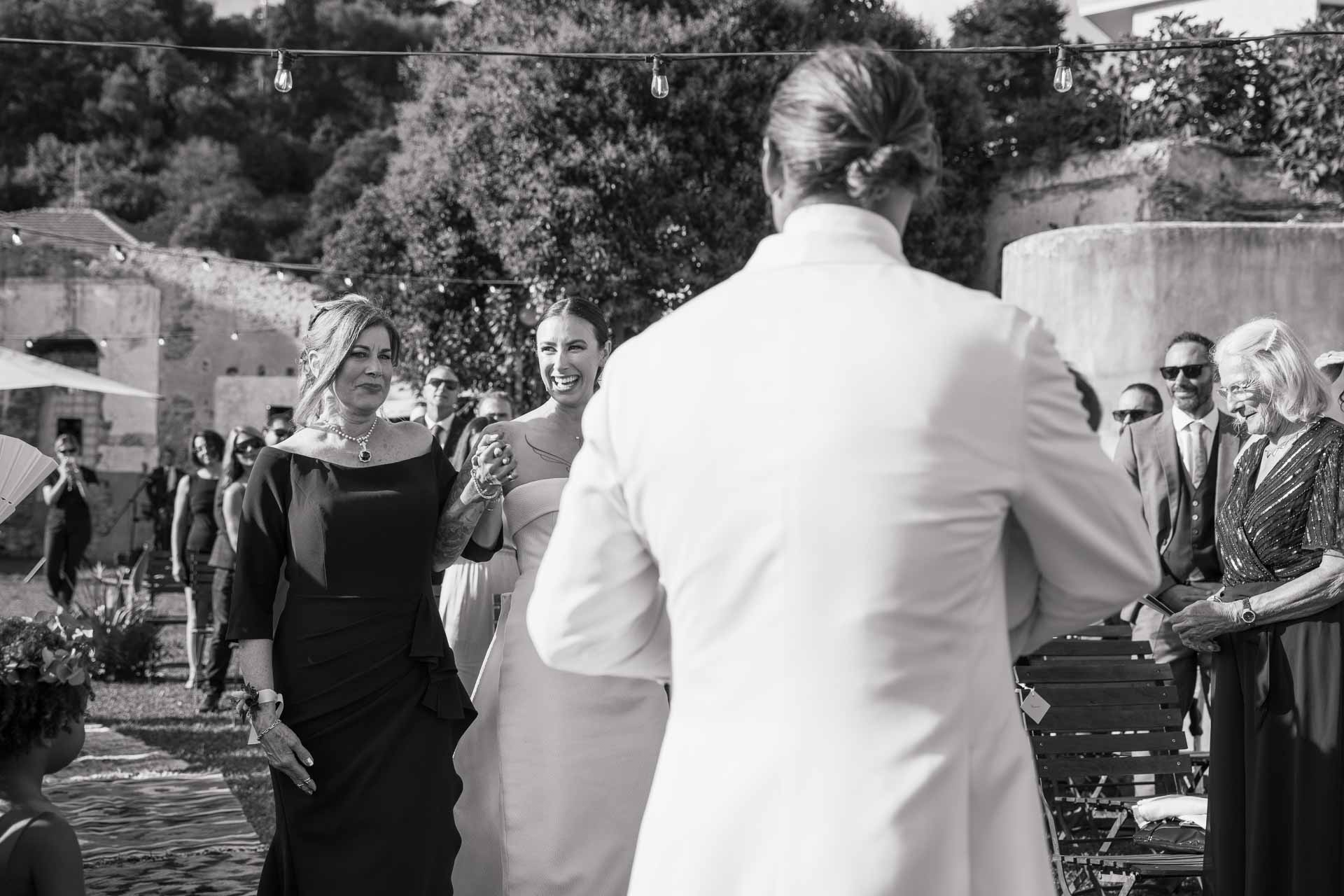 In bianco e nero, lo sposo di spalle guarda arrivare la sposa tra gli invitati