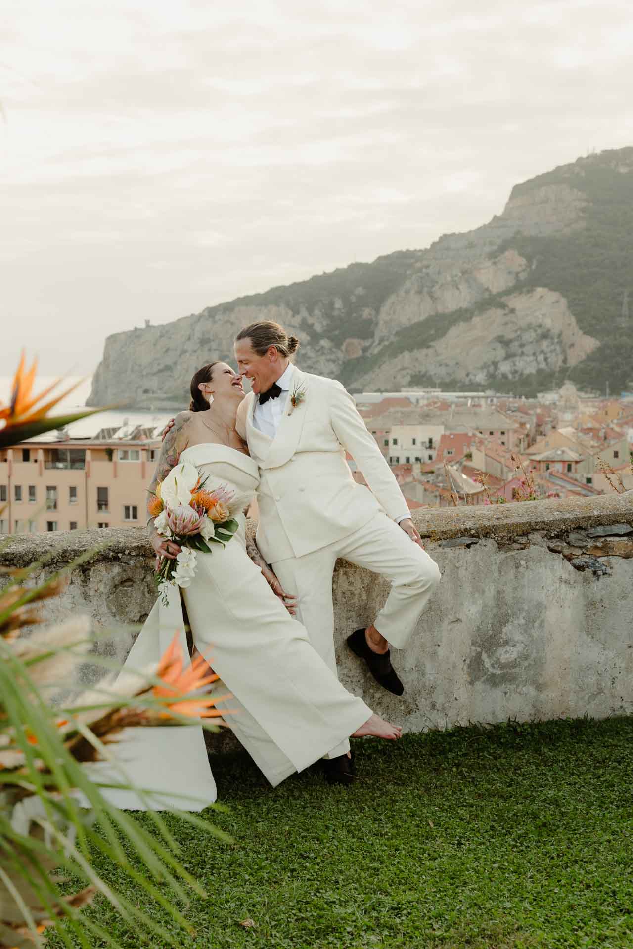 Gli sposi si baciano sul parapetto, con i tetti di Finale e il promontorio alle spalle