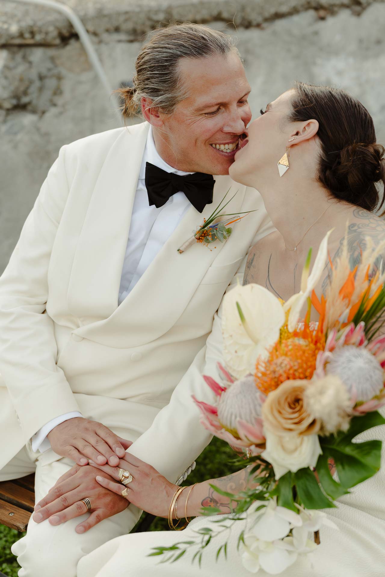 La sposa bacia lo sposo, seduti sul prato con il bouquet in grembo