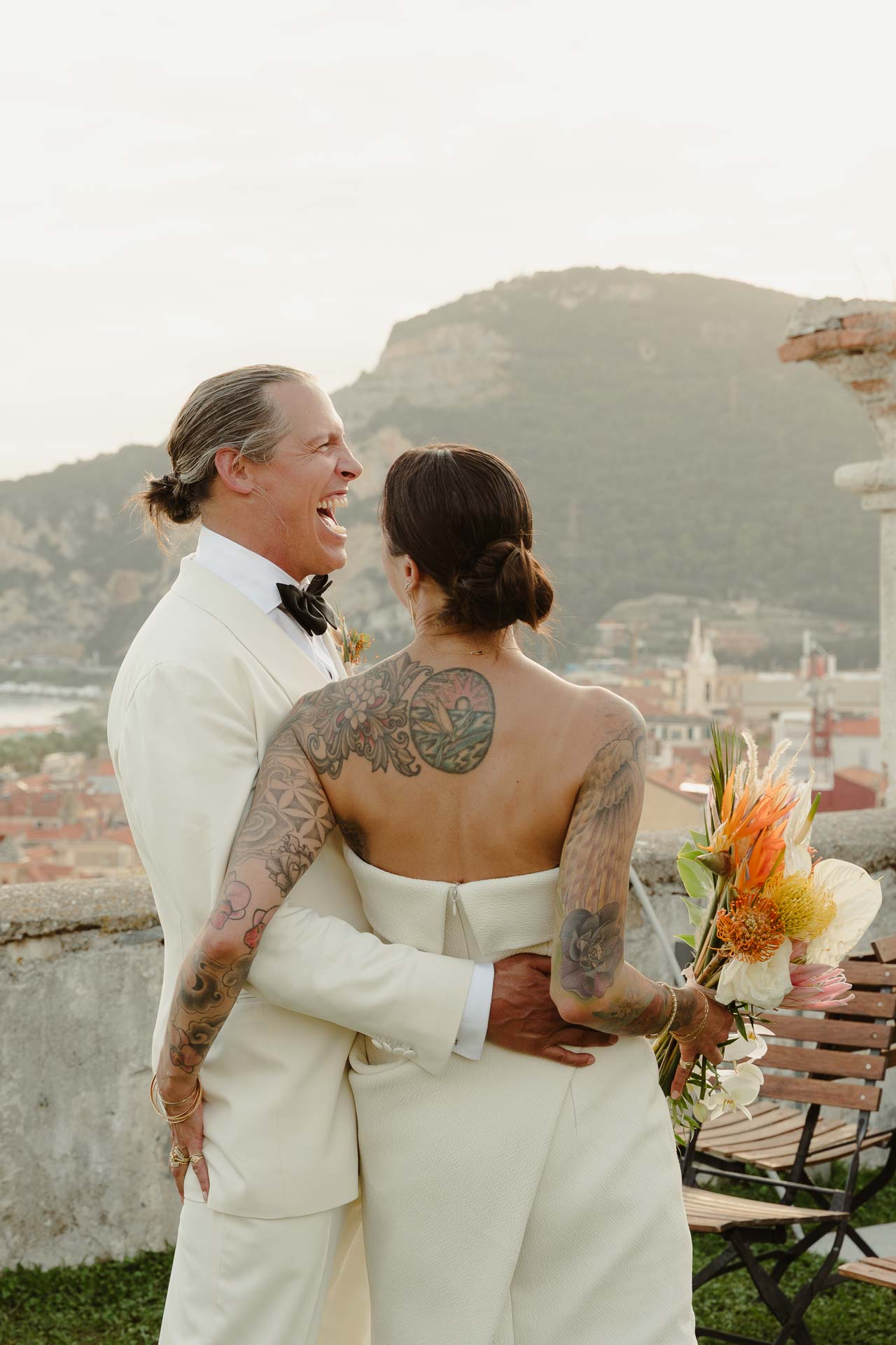 Gli sposi abbracciati sul bastione della fortezza, a Finale Ligure, con la schiena tatuata della sposa e il promontorio sullo sfondo