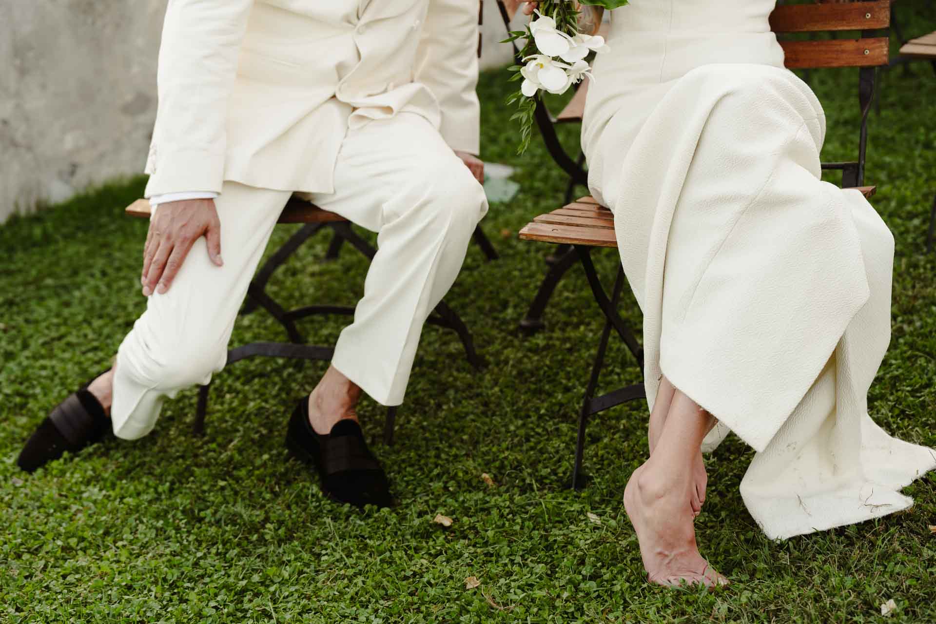 Gli sposi seduti sulle sedie di legno, la sposa a piedi nudi sul prato