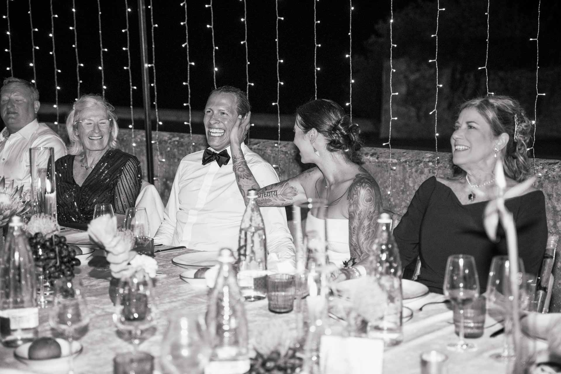 In bianco e nero, gli sposi ridono a tavola con gli invitati
