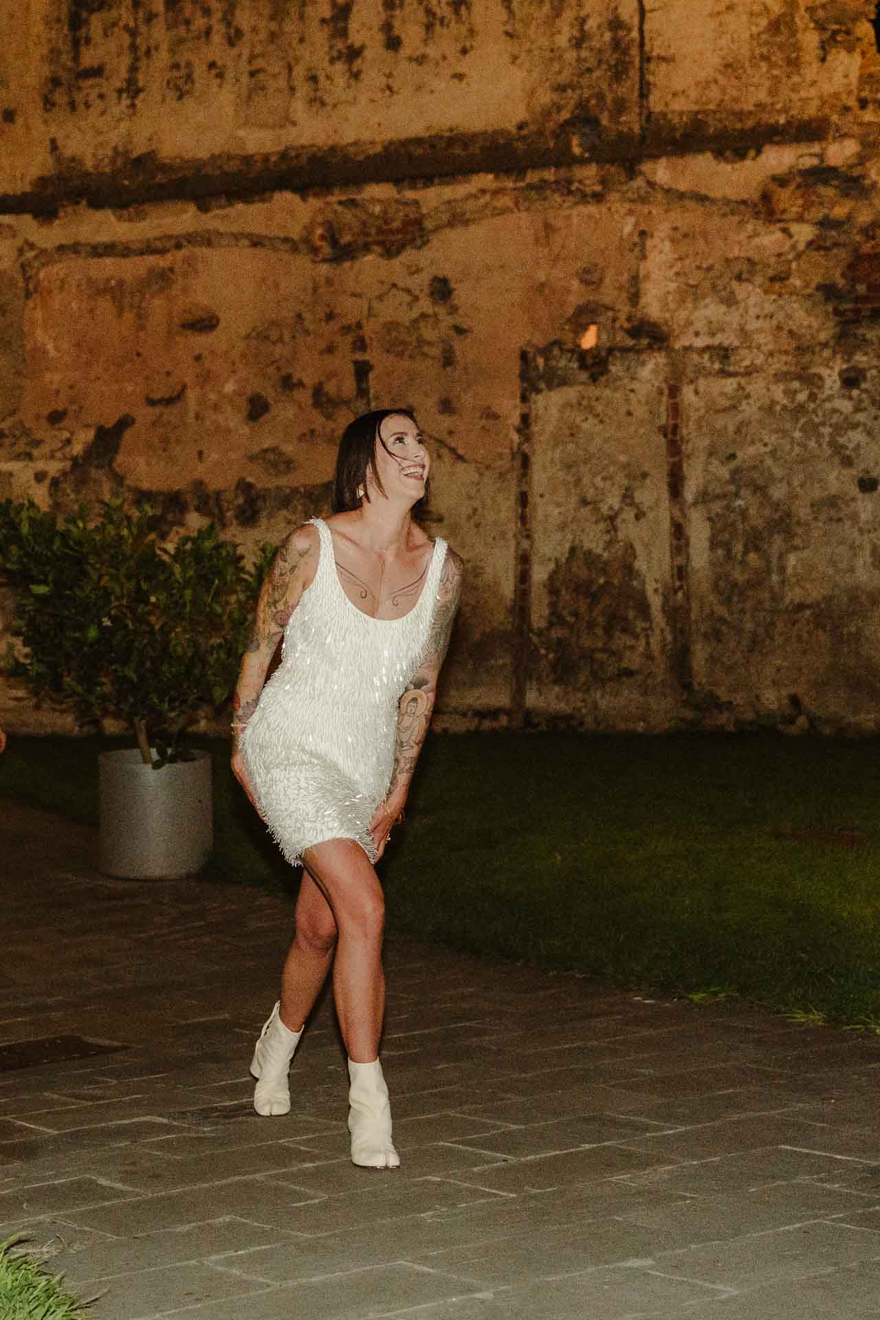 La sposa con il caschetto e l'abito corto a frange balla sul selciato