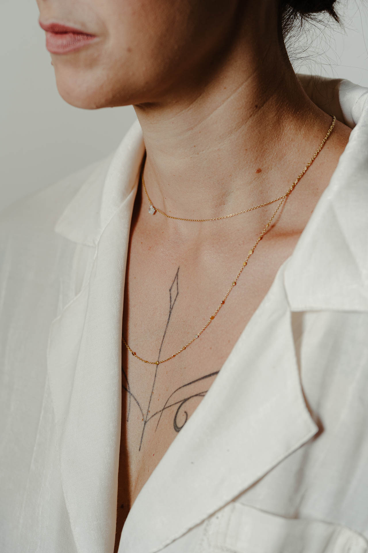 Il collo della sposa con le collane sottili e un tatuaggio, nella vestaglia bianca