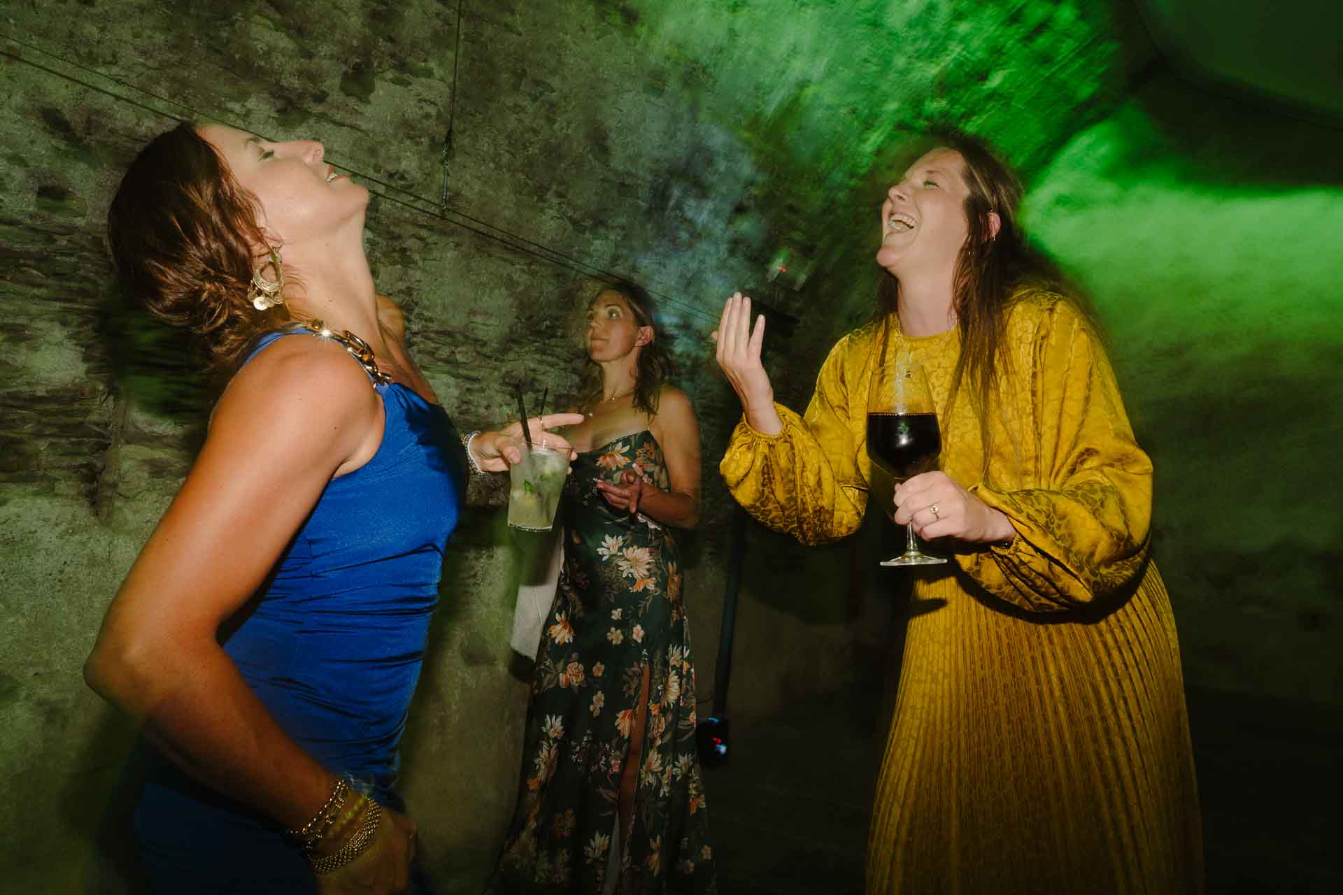 Le invitate ballano e ridono sotto le volte di pietra illuminate di verde