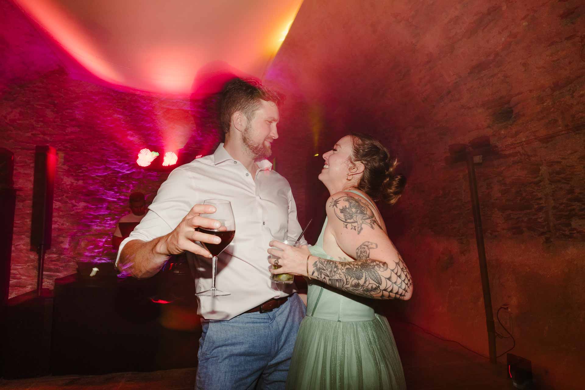 Due invitati ballano con i calici in mano, nella luce rossa