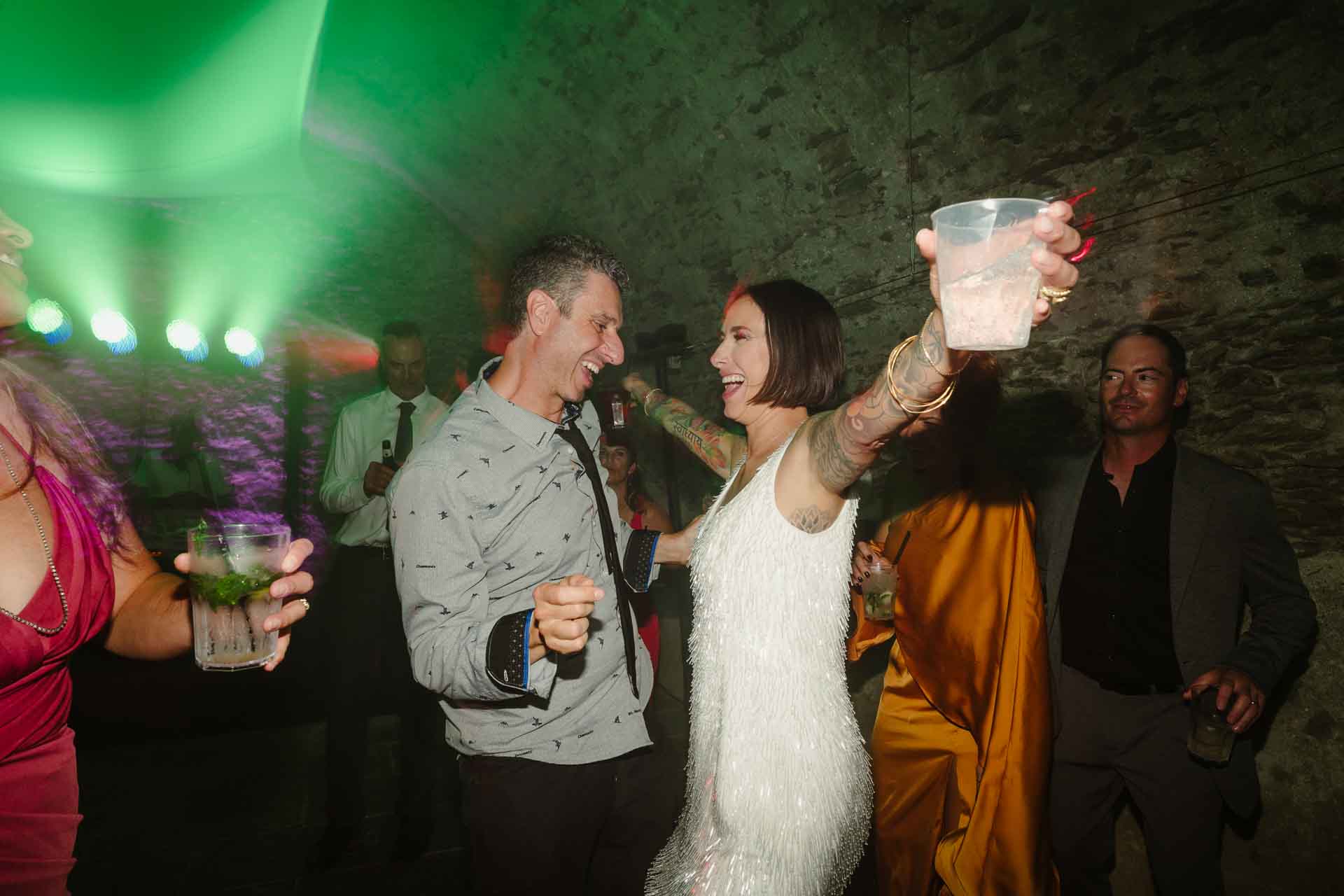 La sposa alza il bicchiere tra gli amici, nella luce verde