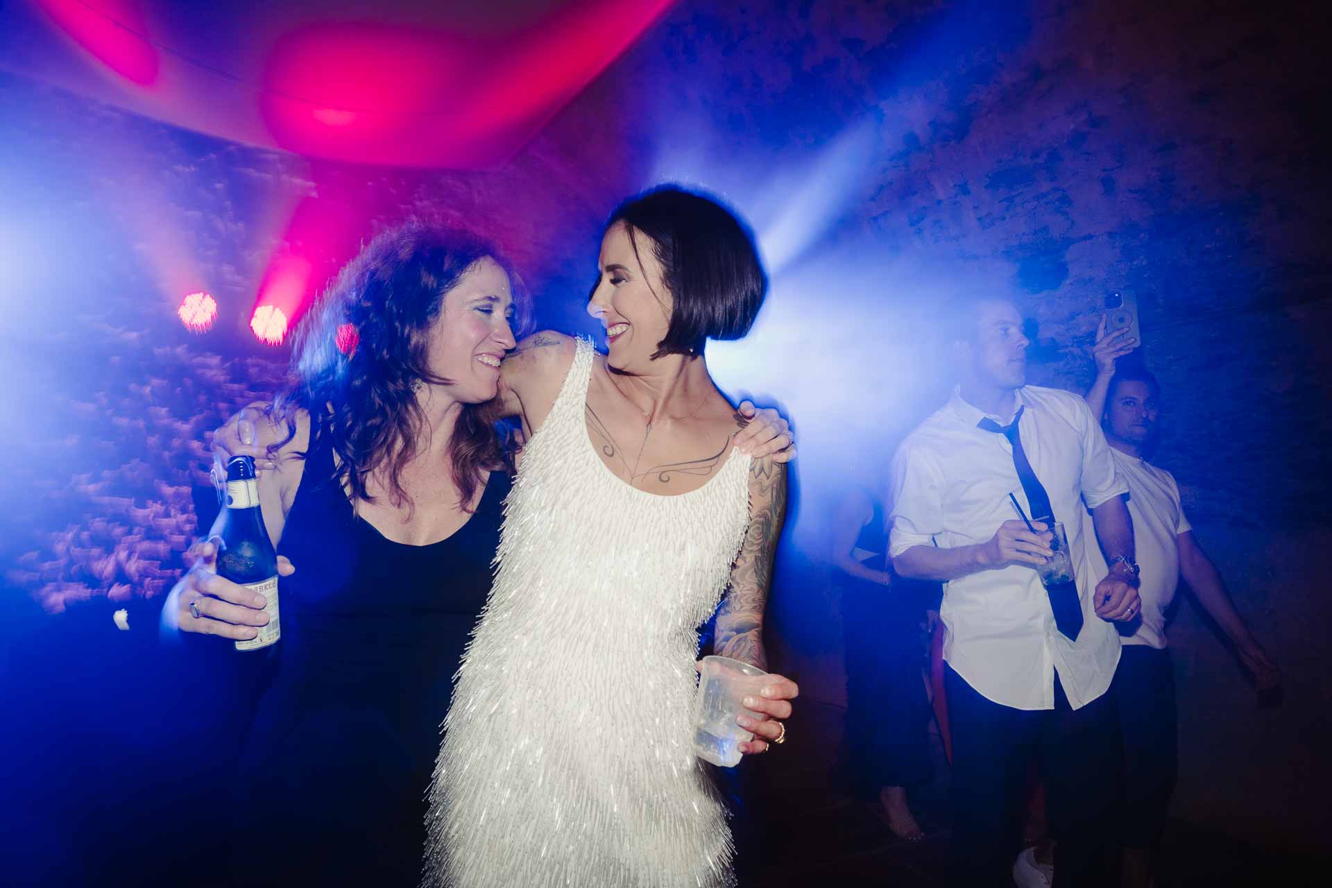 La sposa abbracciata a un'amica, nella luce blu e rossa