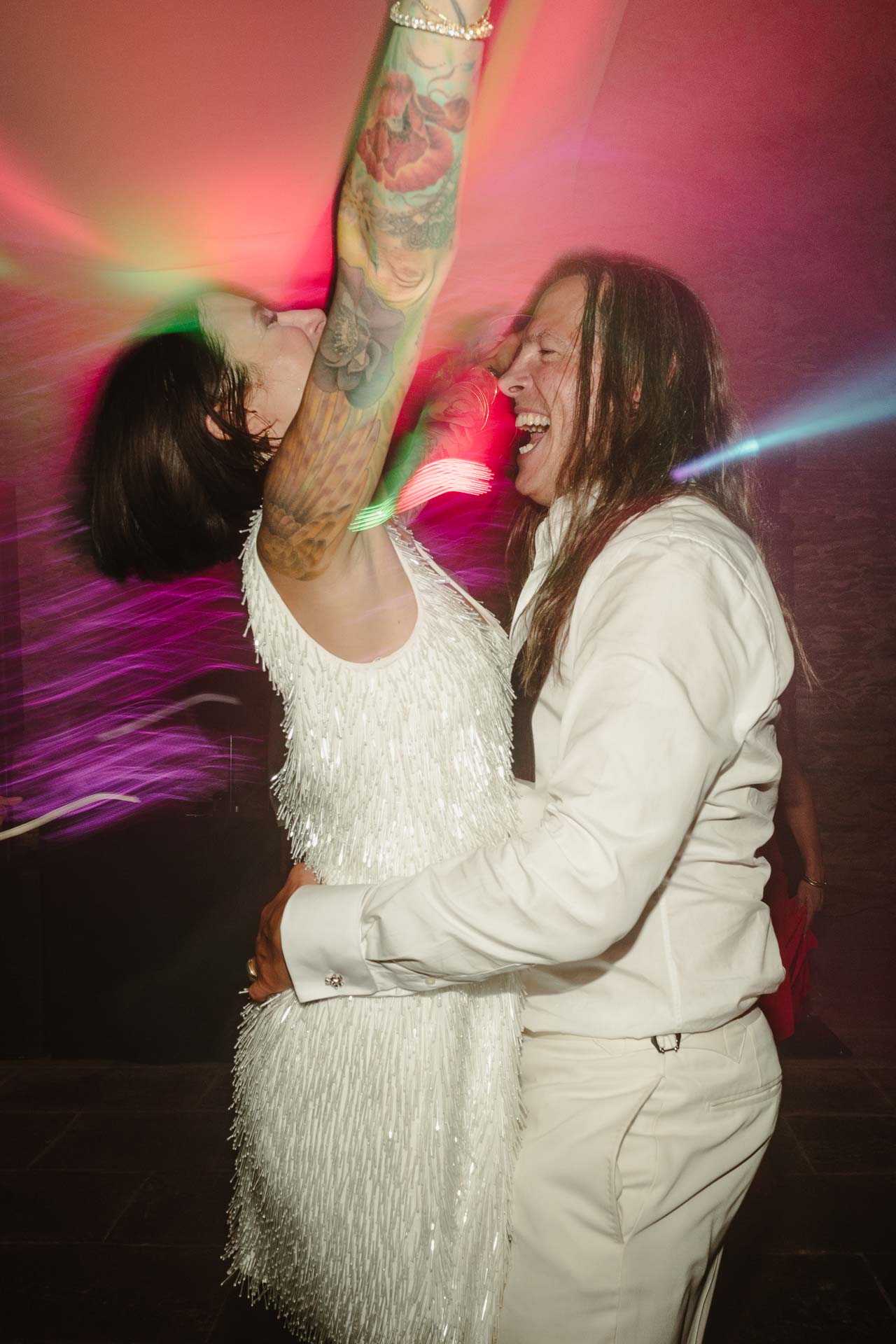 Gli sposi ballano abbracciati, lei alza il braccio tatuato tra le luci colorate