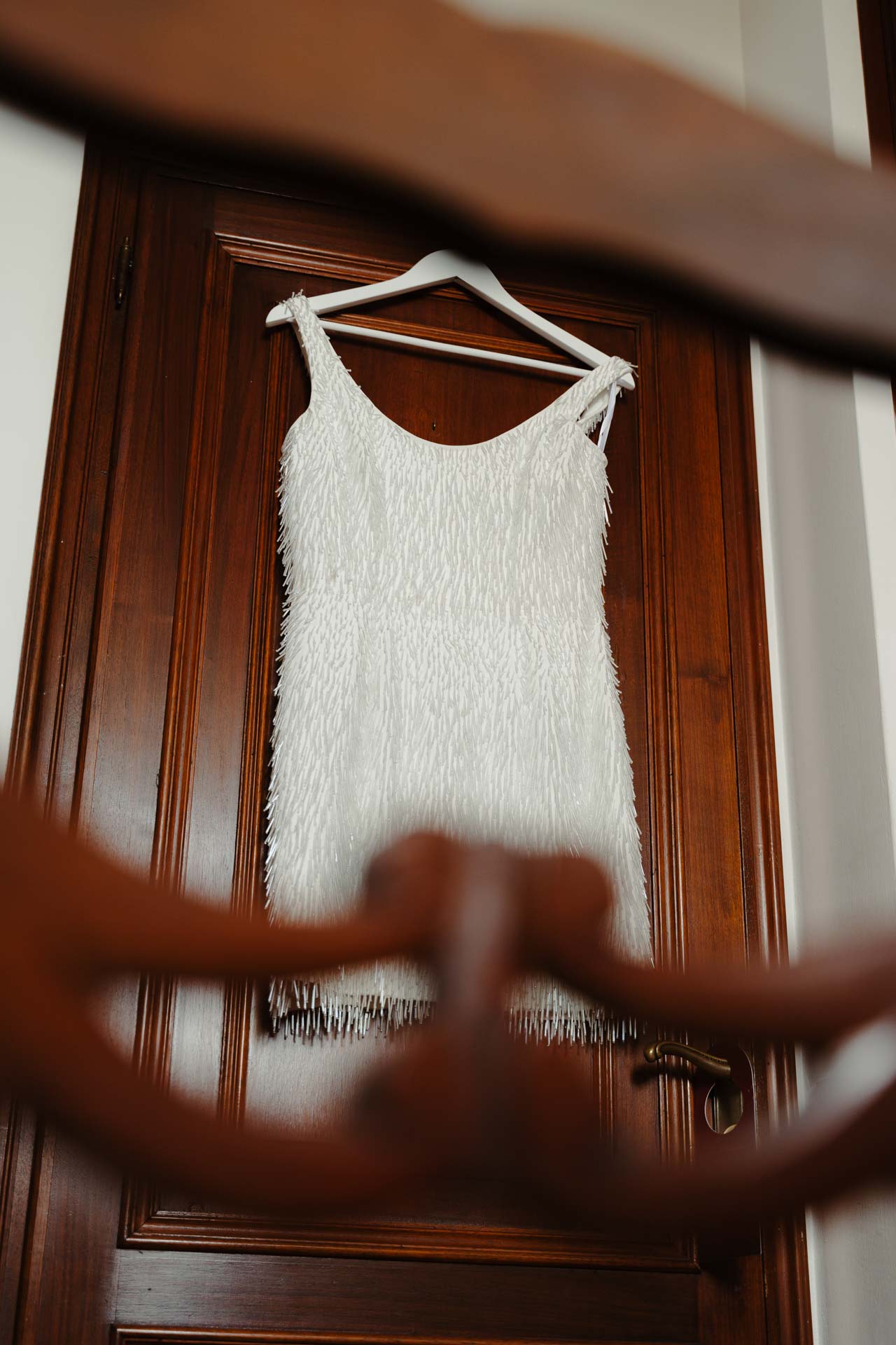 Il secondo abito della sposa, corto e a frange, appeso alla porta di legno
