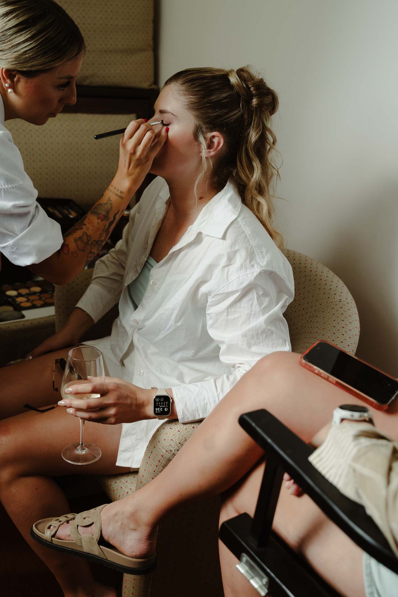 Un'amica della sposa al trucco, con un calice in mano