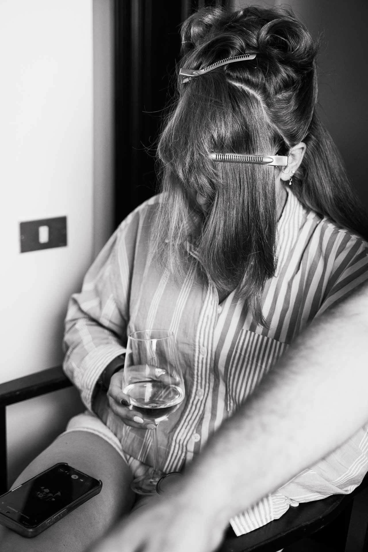 In bianco e nero, un'invitata con i capelli fermati dalle mollette e un calice in mano