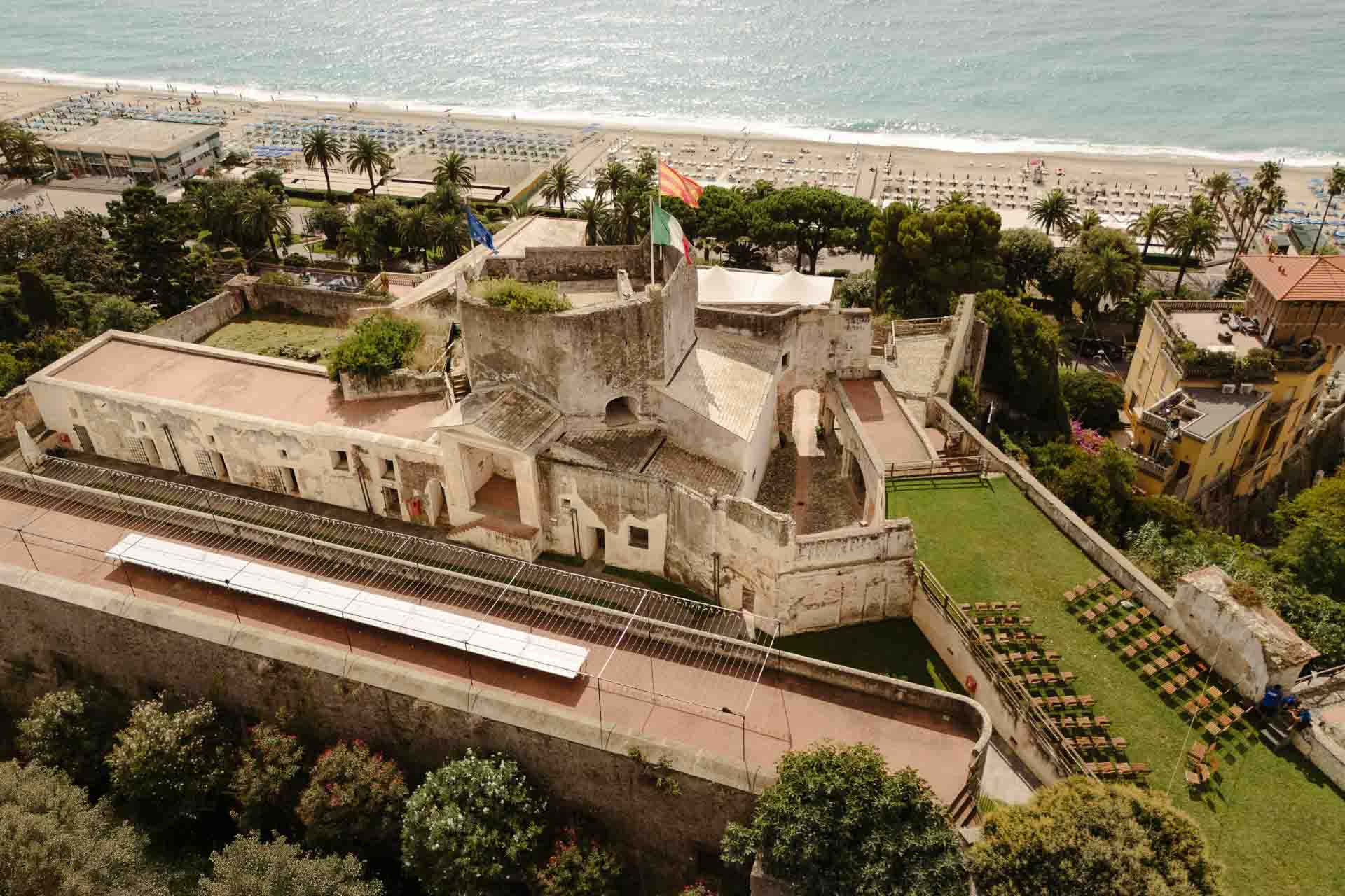 La Fortezza di Castelfranco dall'alto, con il mare e la spiaggia di Finale Ligure alle spalle e le sedie della cerimonia sul prato