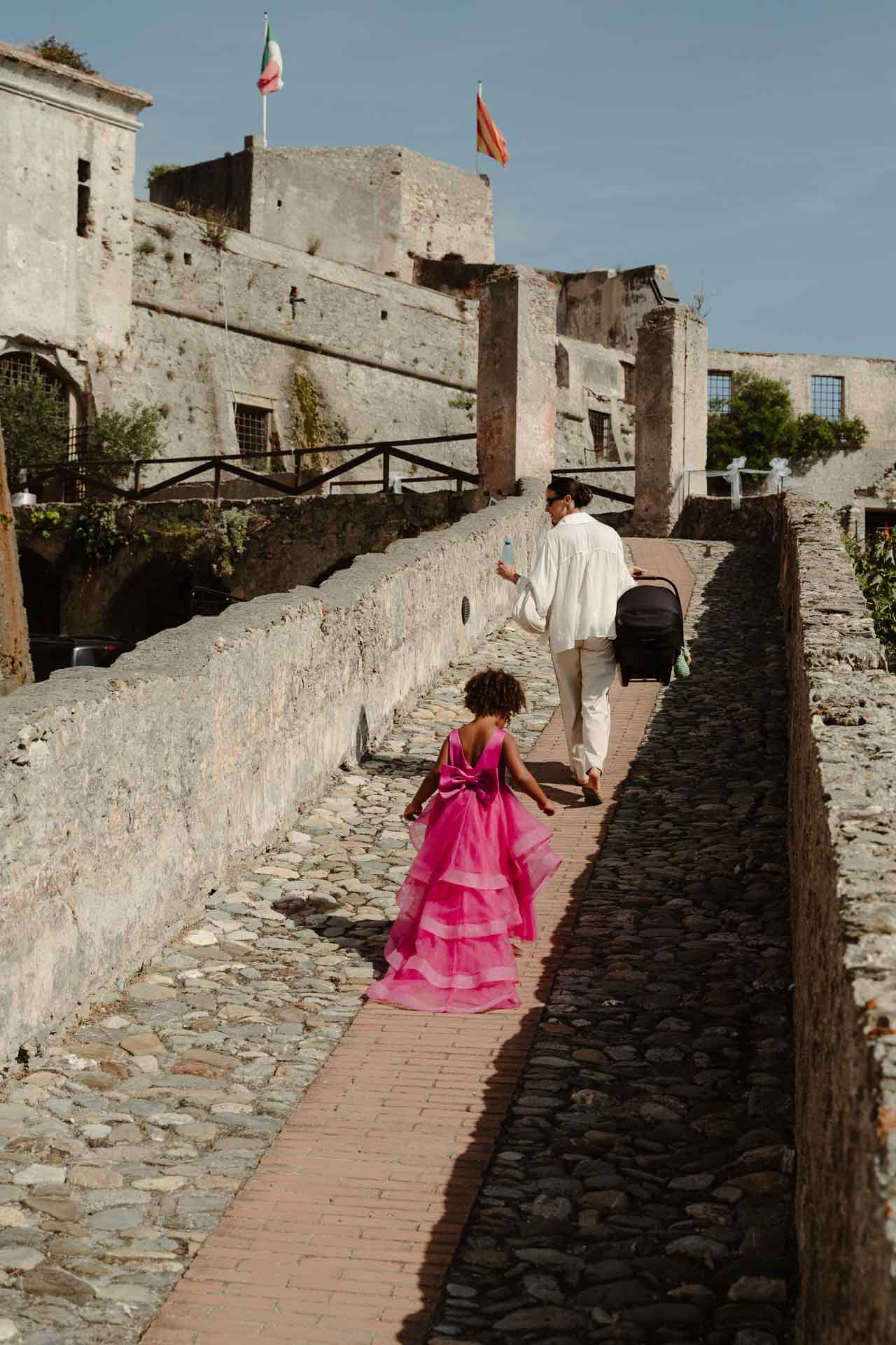 Una bambina in abito fucsia corre sul camminamento di pietra verso la fortezza