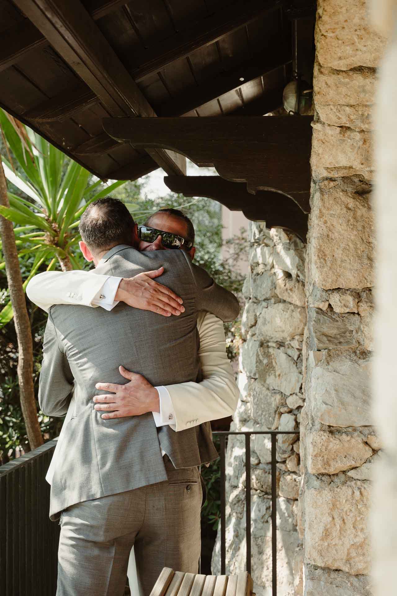 L'abbraccio tra lo sposo e l'amico, sotto la tettoia di legno