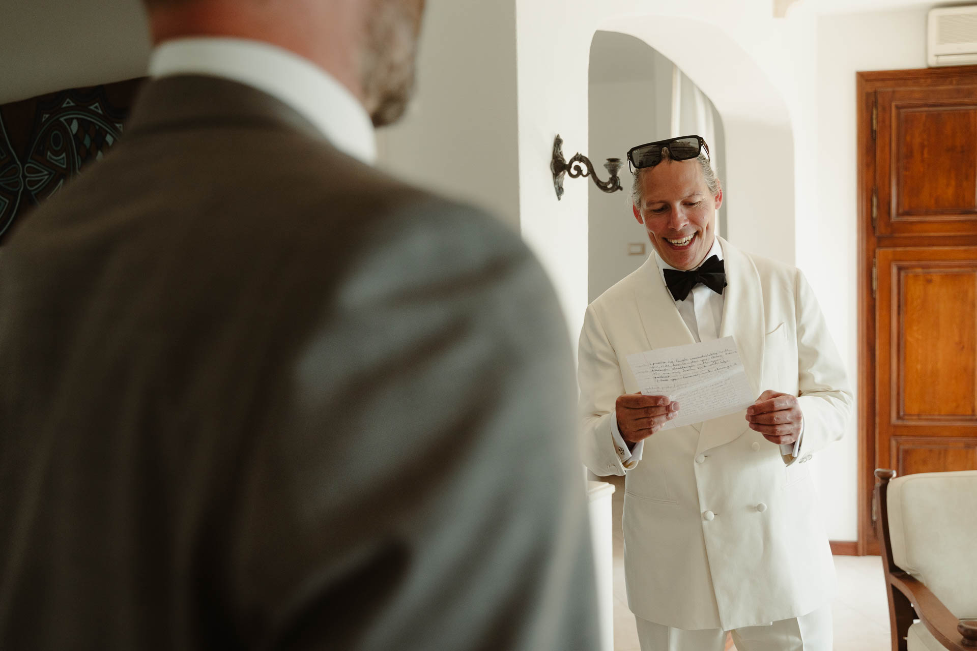 Lo sposo legge un foglio davanti a un amico in abito grigio