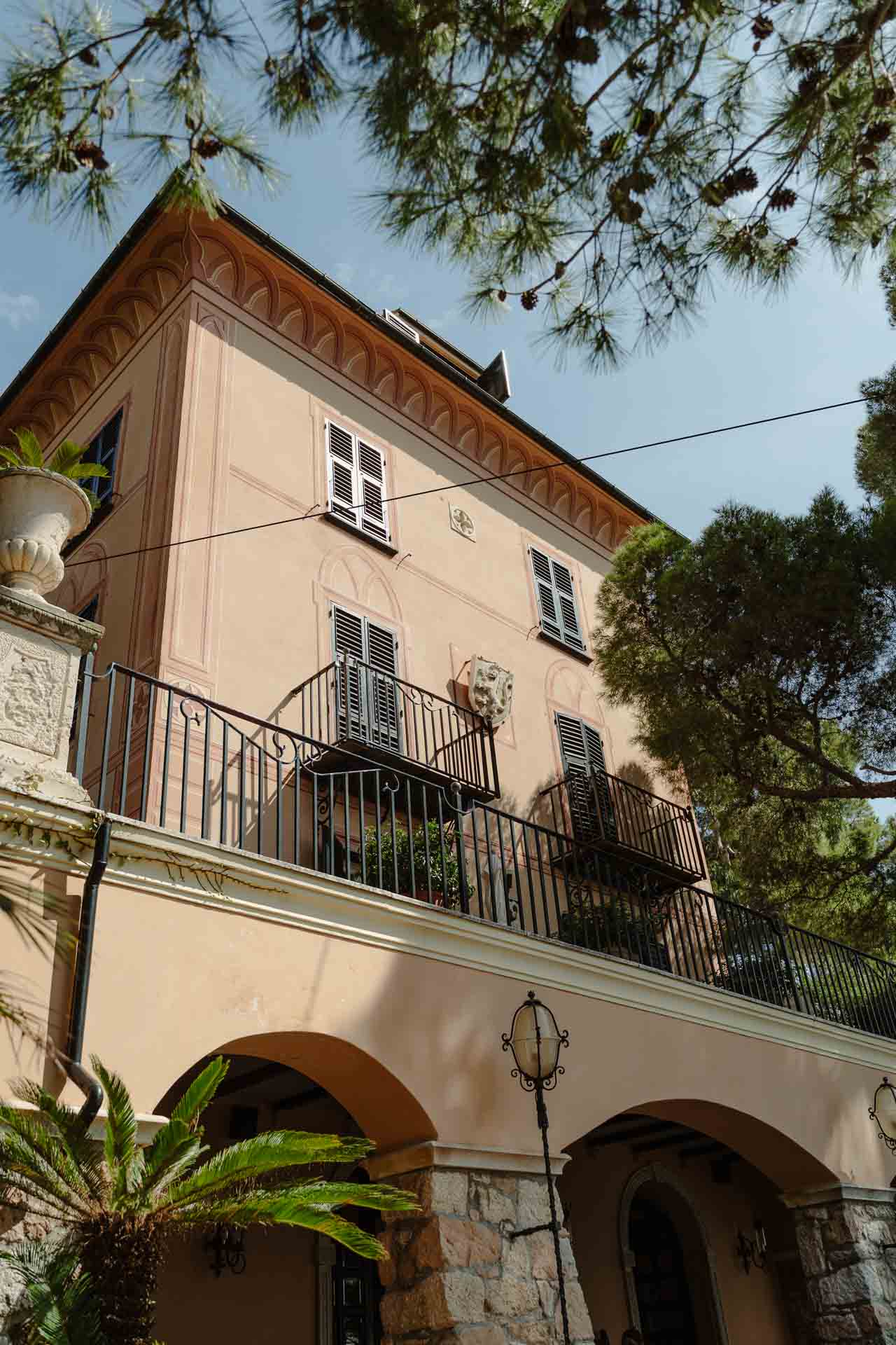 La facciata rosa di una villa con il balcone in ferro, tra i pini