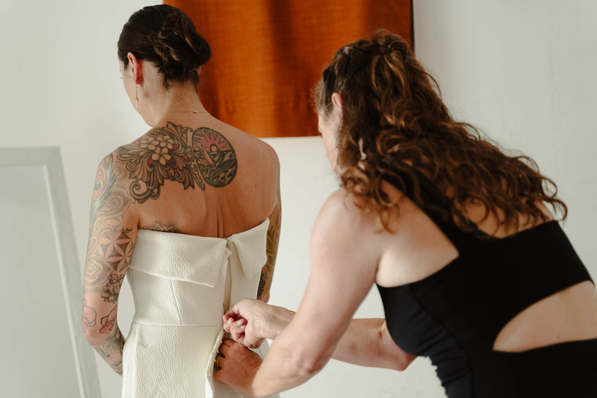 Un'amica chiude l'abito della sposa sulla schiena tatuata