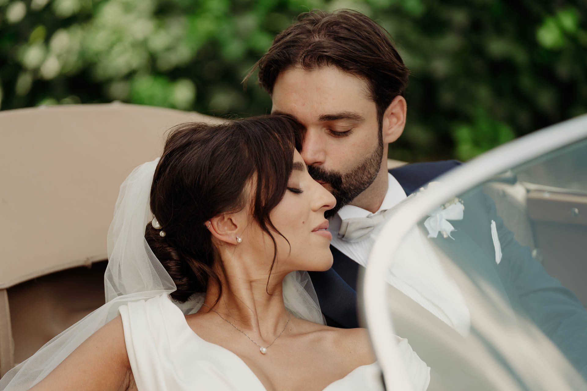 La sposa con gli occhi chiusi, appoggiata allo sposo sul sedile dell'auto d'epoca