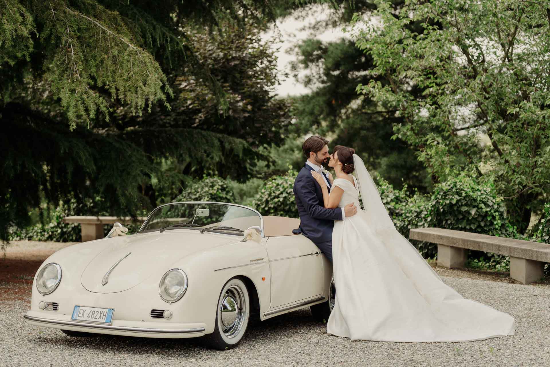 Gli sposi si abbracciano accanto all'auto d'epoca bianca, nel parco di Villa Cimena