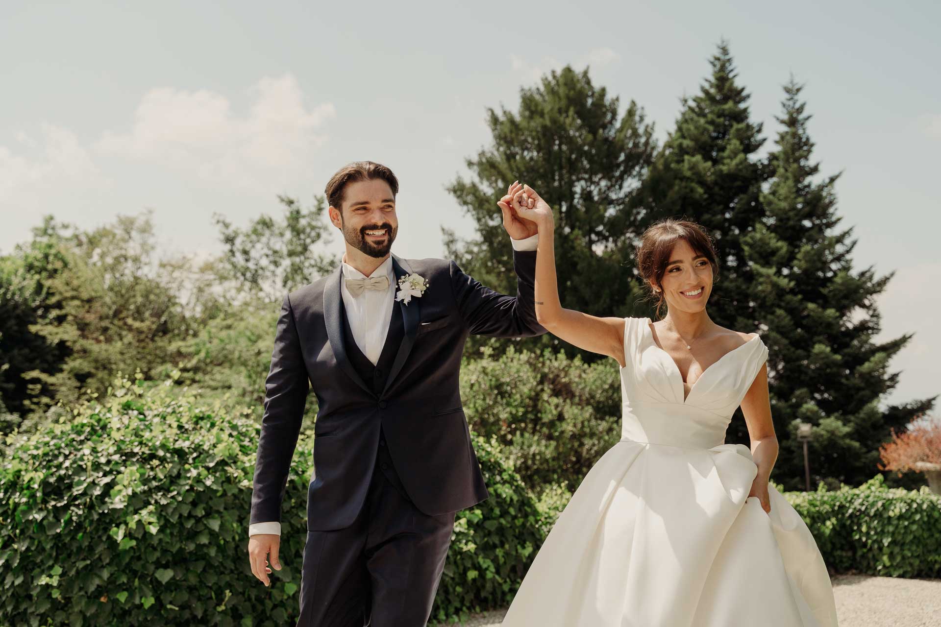 Lo sposo alza il braccio della sposa in segno di festa, tra le siepi