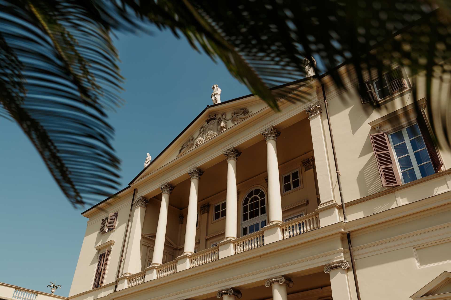 La facciata di Villa Cimena con le colonne, sotto il cielo blu e le foglie di palma
