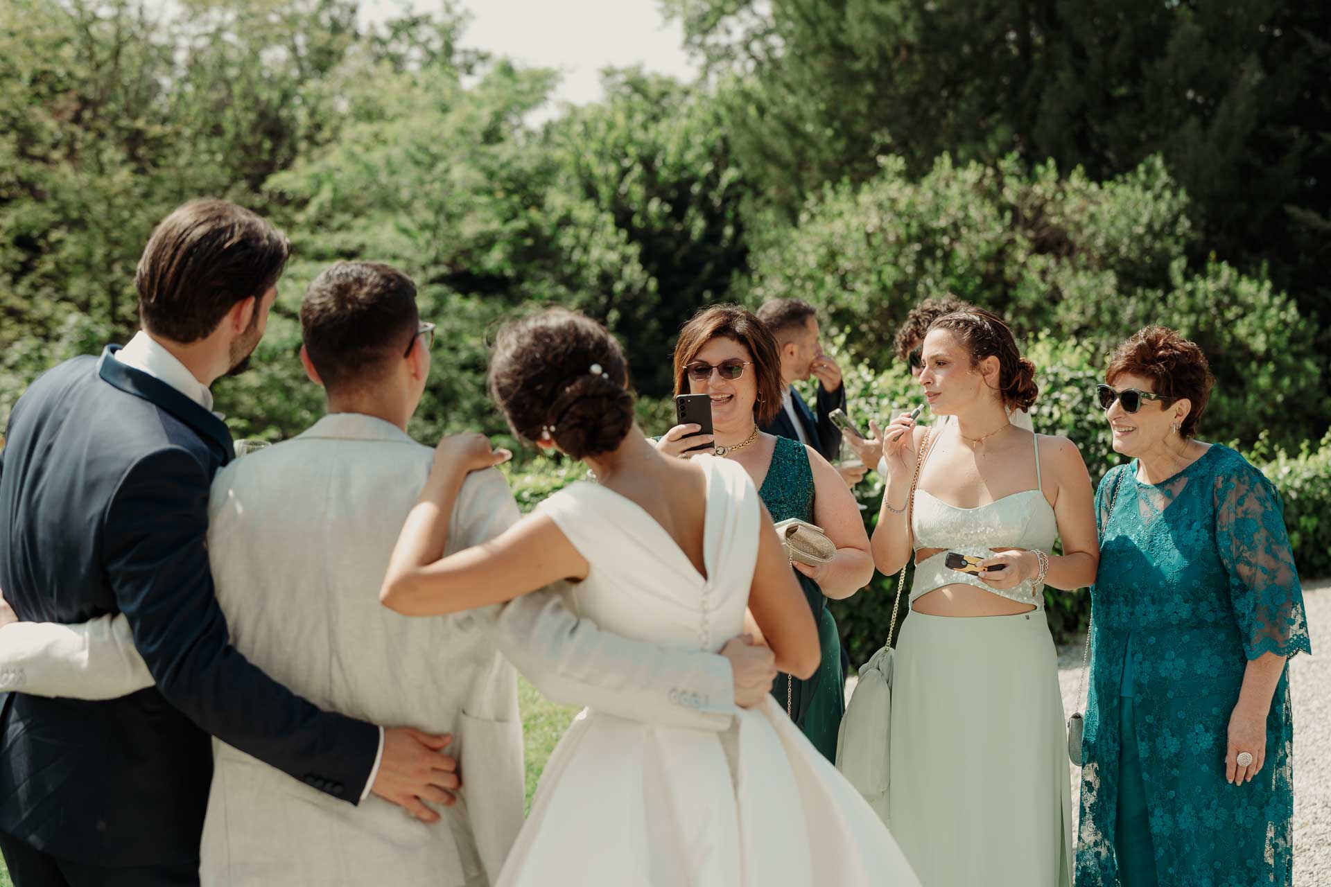 La sposa abbraccia gli amici nel giardino, di spalle, con le invitate che ridono
