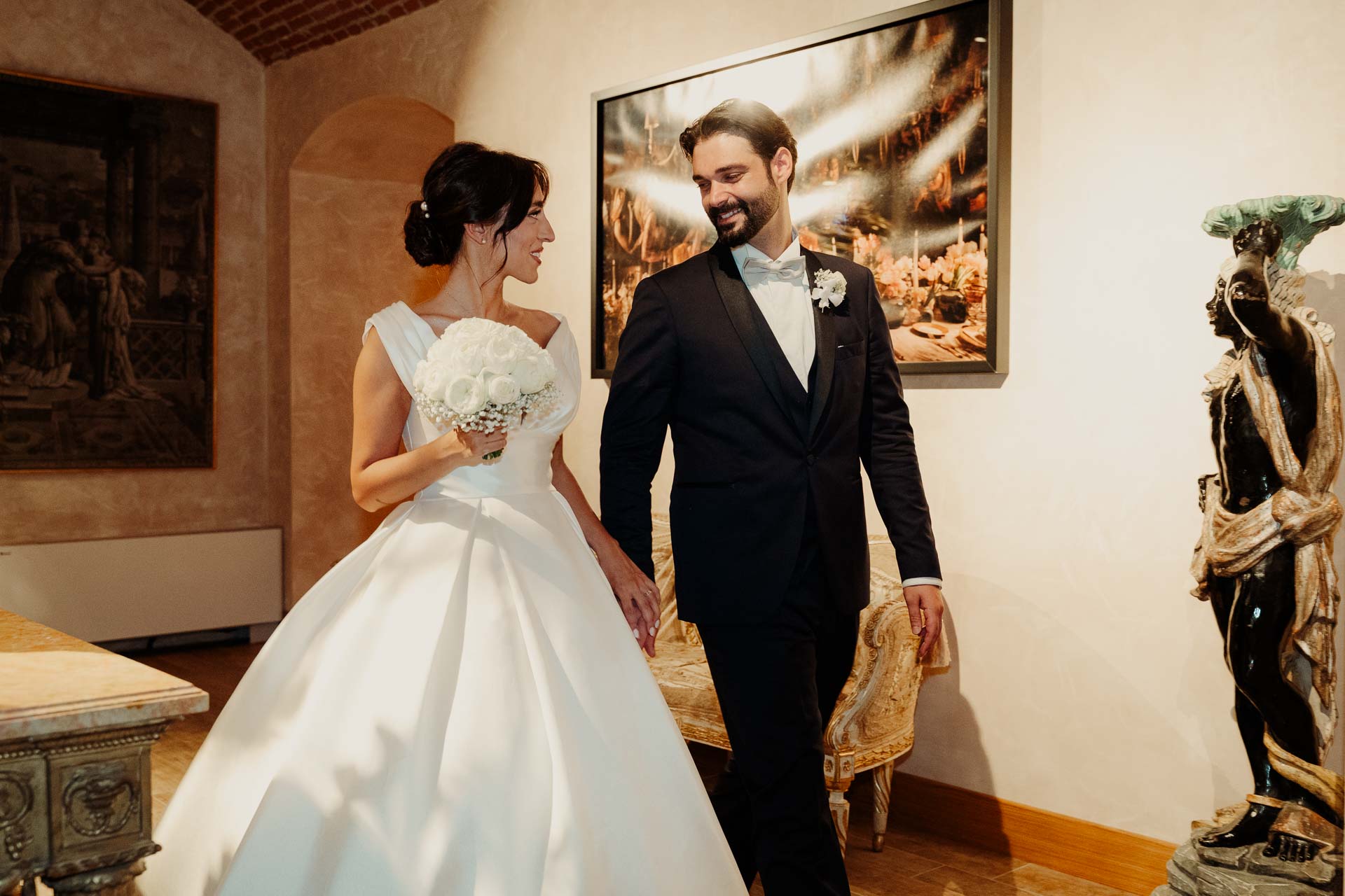 Gli sposi camminano sorridenti nel salone della villa, con il bouquet in mano