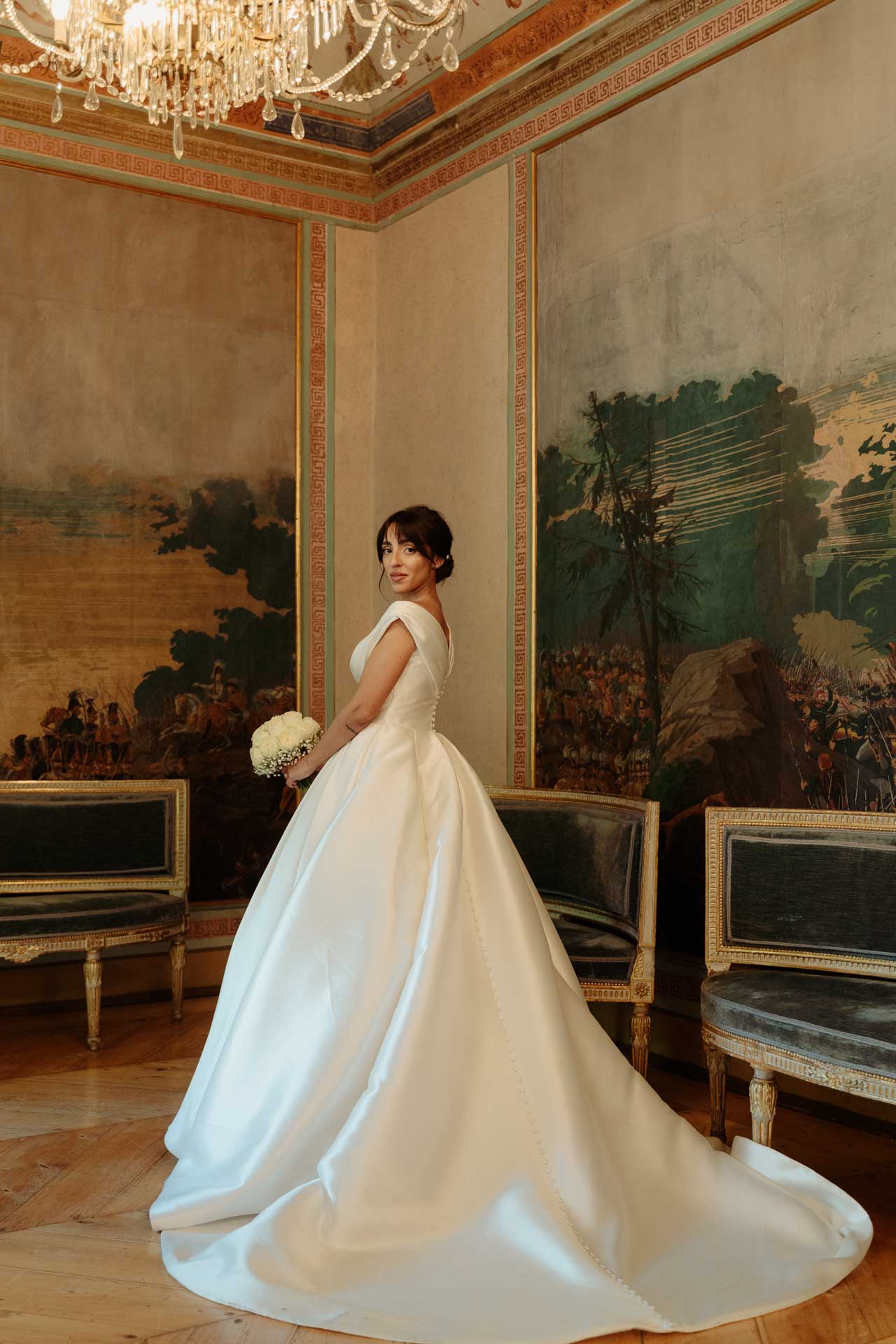 La sposa di profilo con il bouquet, nel salone affrescato con le sedie azzurre