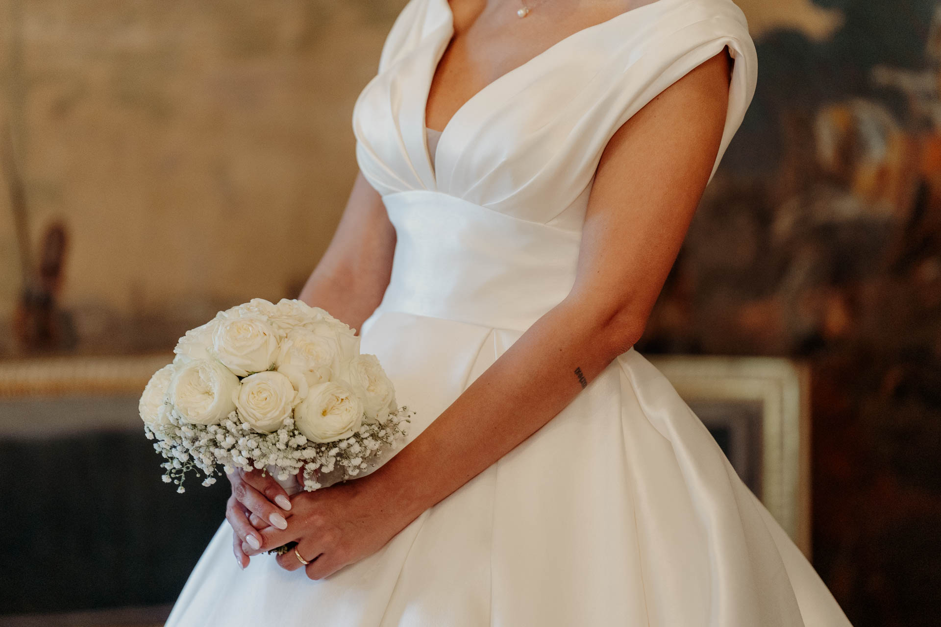 Dettaglio dell'abito con scollo a V e del bouquet di rose bianche tenuto in mano dalla sposa