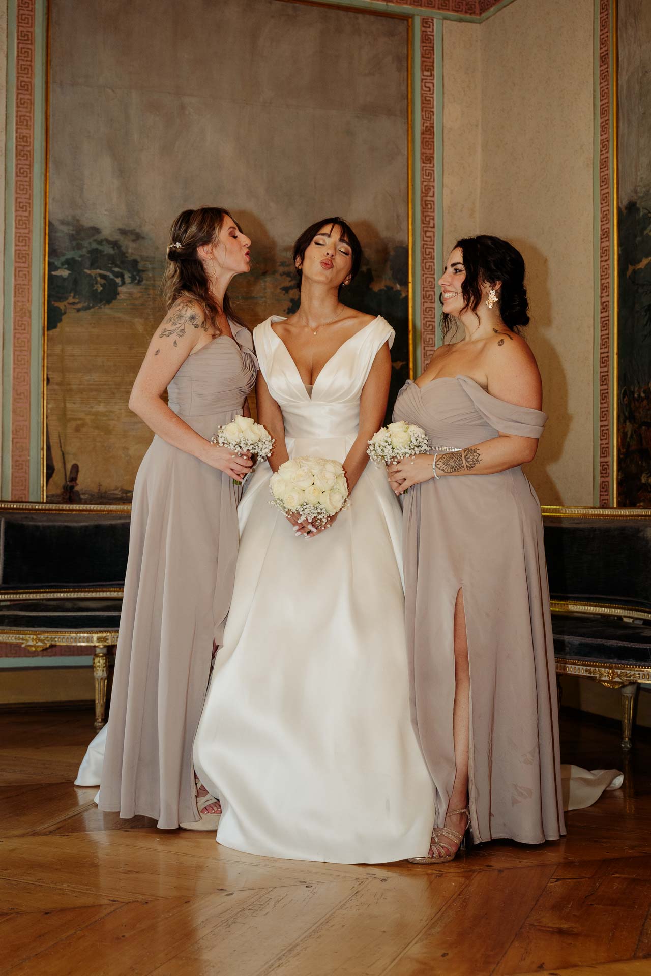 La sposa tra le due damigelle in abito color cipria, nel salone affrescato