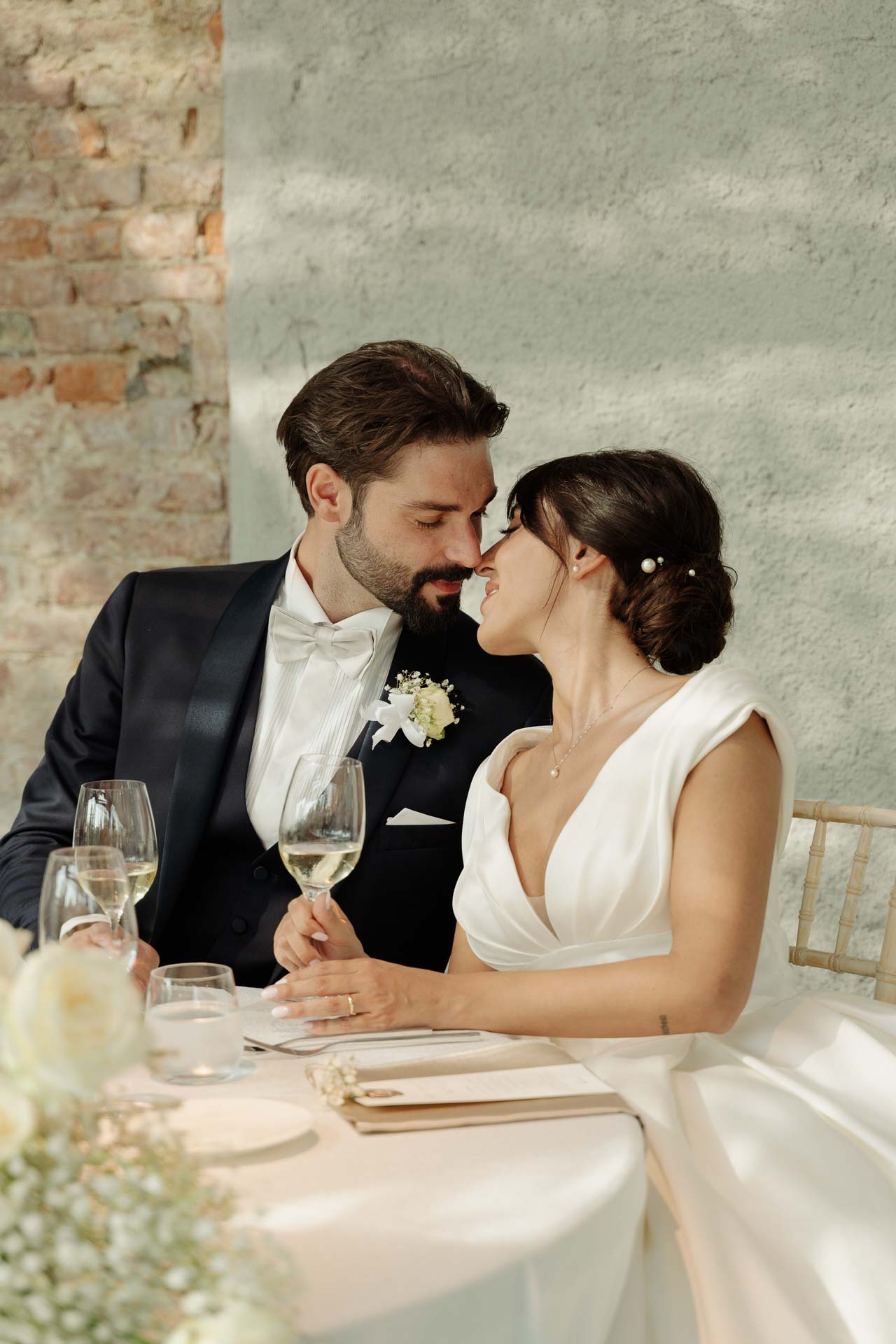 Gli sposi si baciano al loro tavolo, con i calici di vino bianco davanti