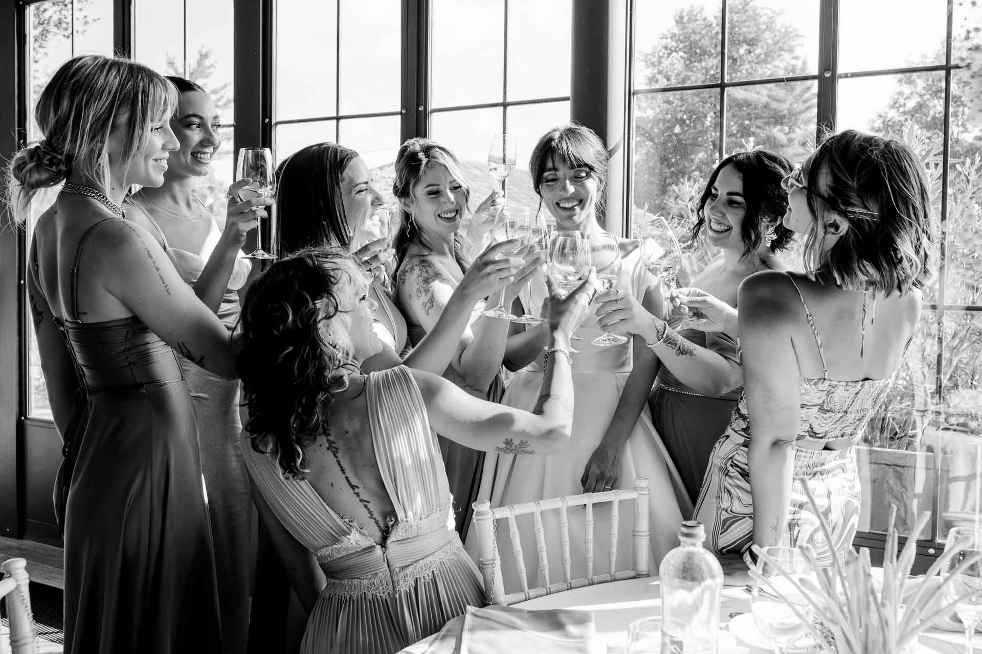 In bianco e nero, le amiche brindano abbracciate davanti alle vetrate