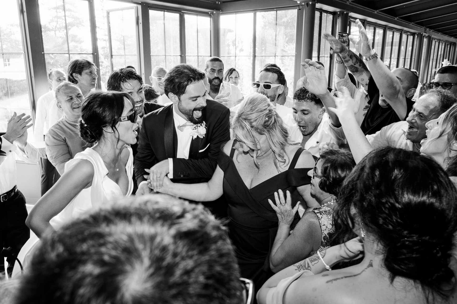 In bianco e nero, la sposa ride tra le braccia degli invitati stretti intorno a lei