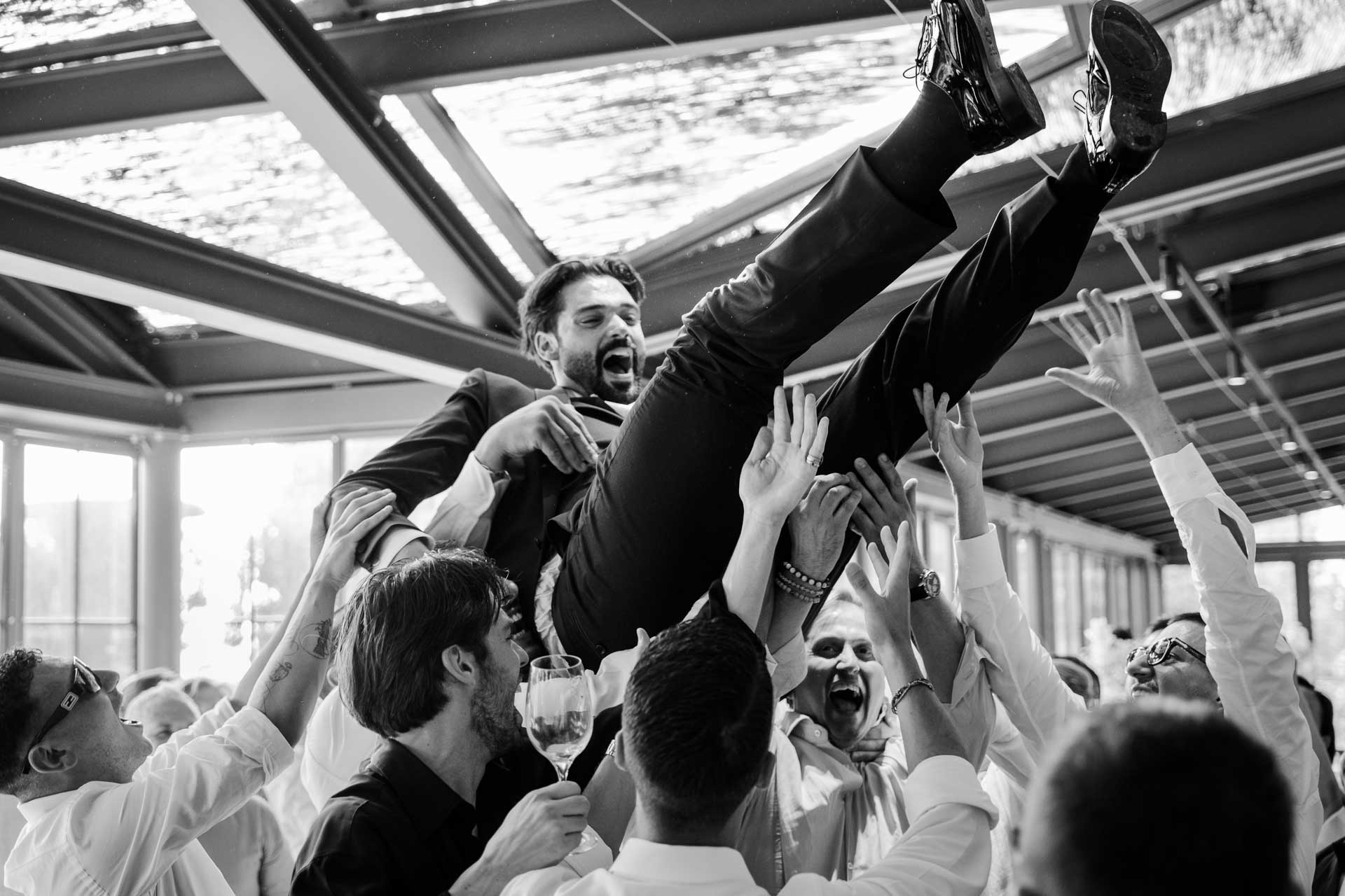 In bianco e nero, lo sposo viene lanciato in aria dagli amici sotto il tetto di vetro