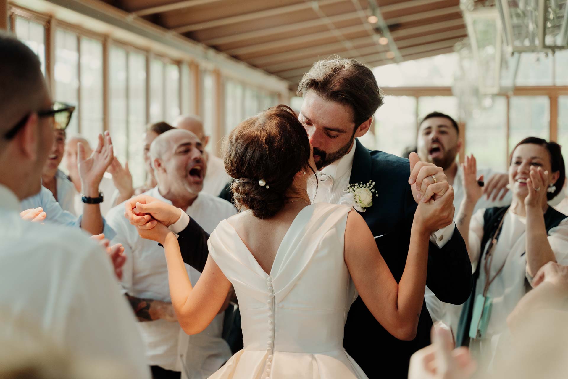 La sposa e lo sposo si baciano tra gli invitati che battono le mani