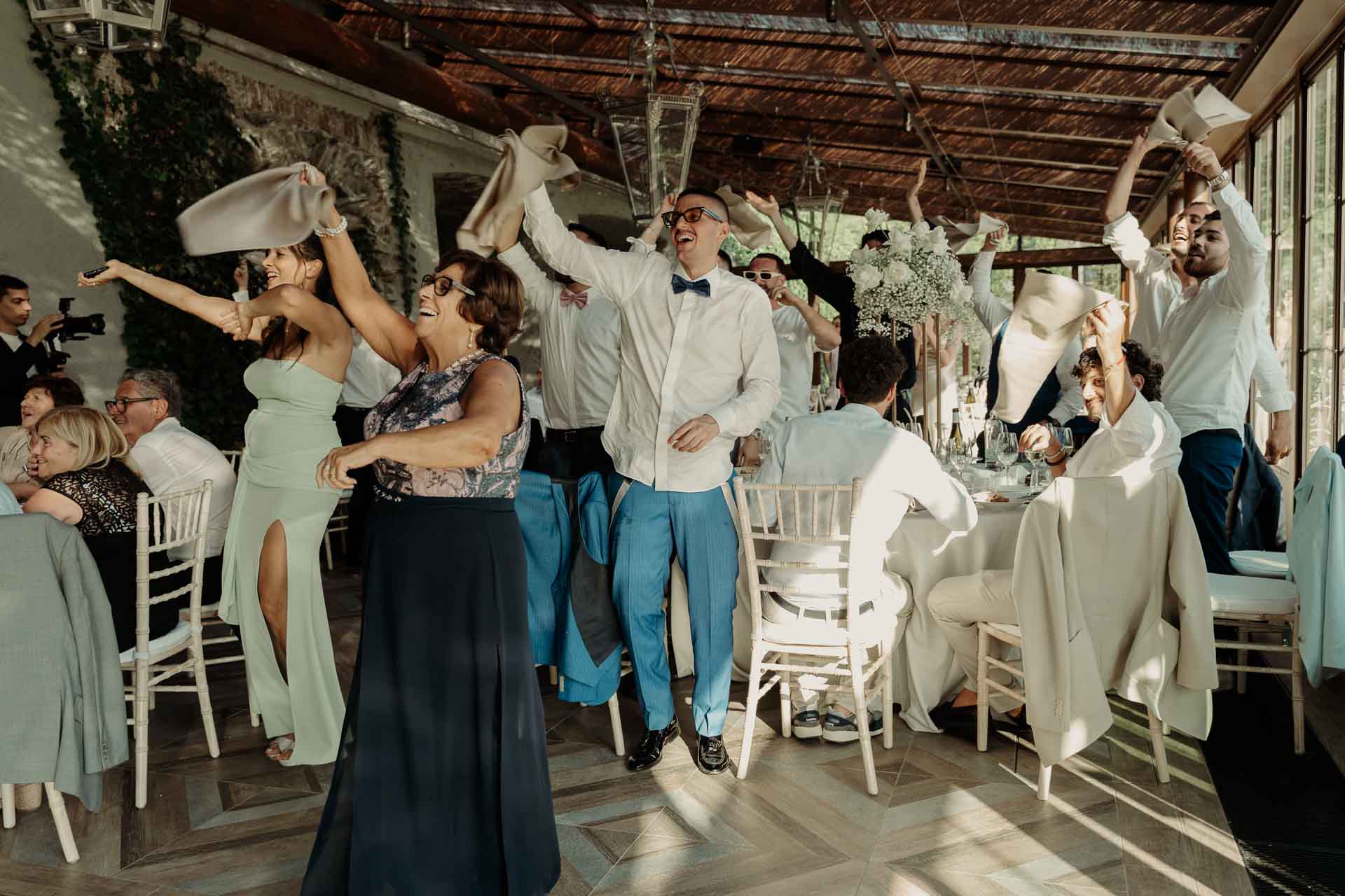 Gli invitati ballano e agitano i tovaglioli tra i tavoli della veranda