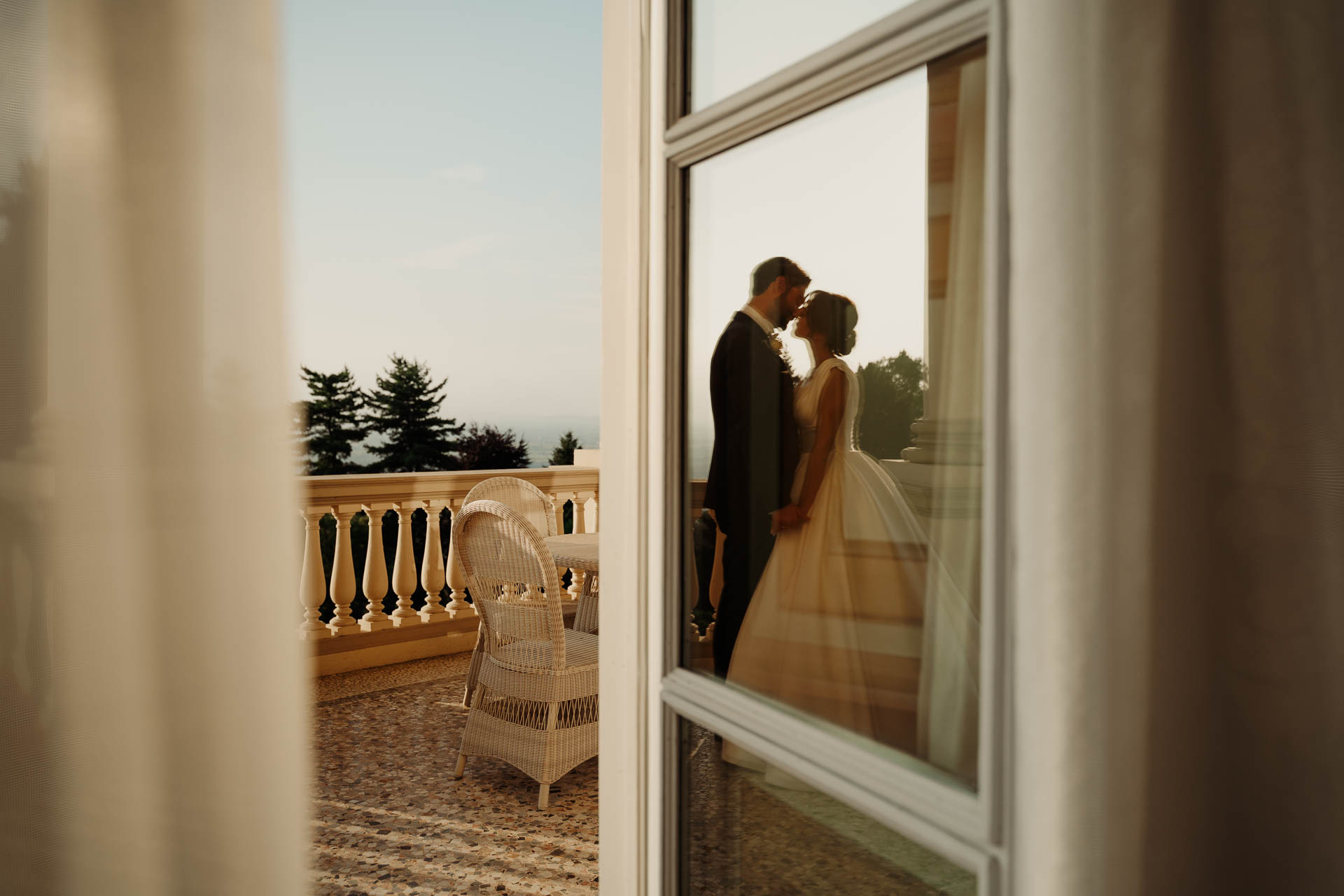 Gli sposi riflessi nel vetro della finestra, con la balconata e le colline fuori