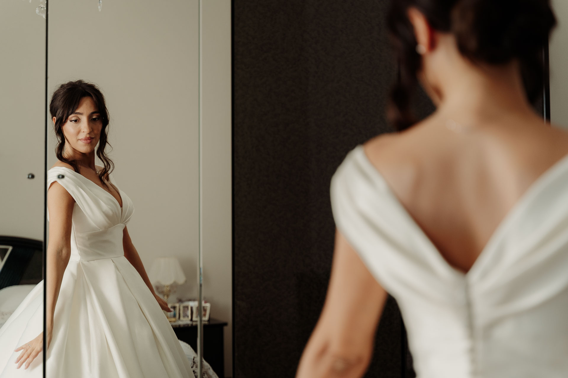La sposa di profilo nello specchio e, in primo piano, la schiena dell'abito a V