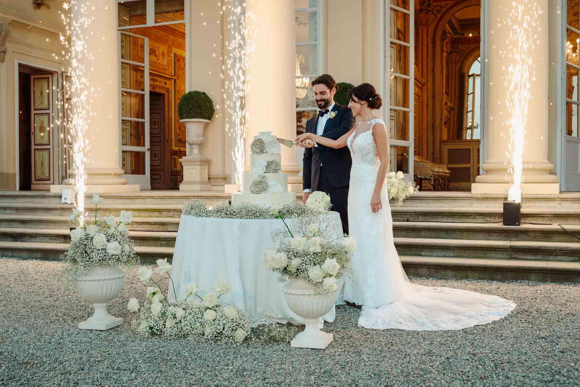 Gli sposi tagliano la torta davanti ai gradini di Villa Cimena, tra le fontane di scintille