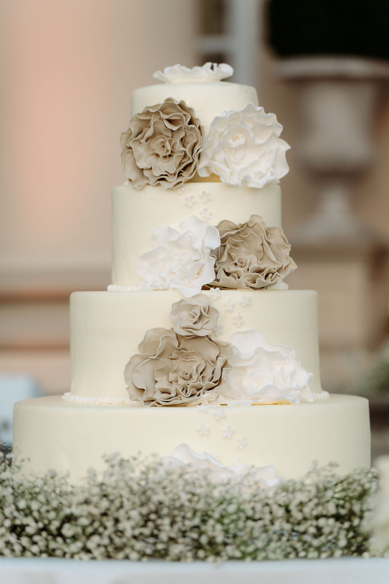 La torta a più piani con i fiori di zucchero color tortora e bianchi, su un letto di gypsophila
