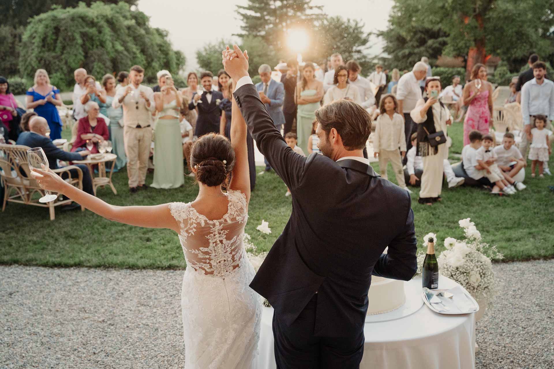 Gli sposi di spalle alzano le braccia davanti agli invitati radunati sul prato