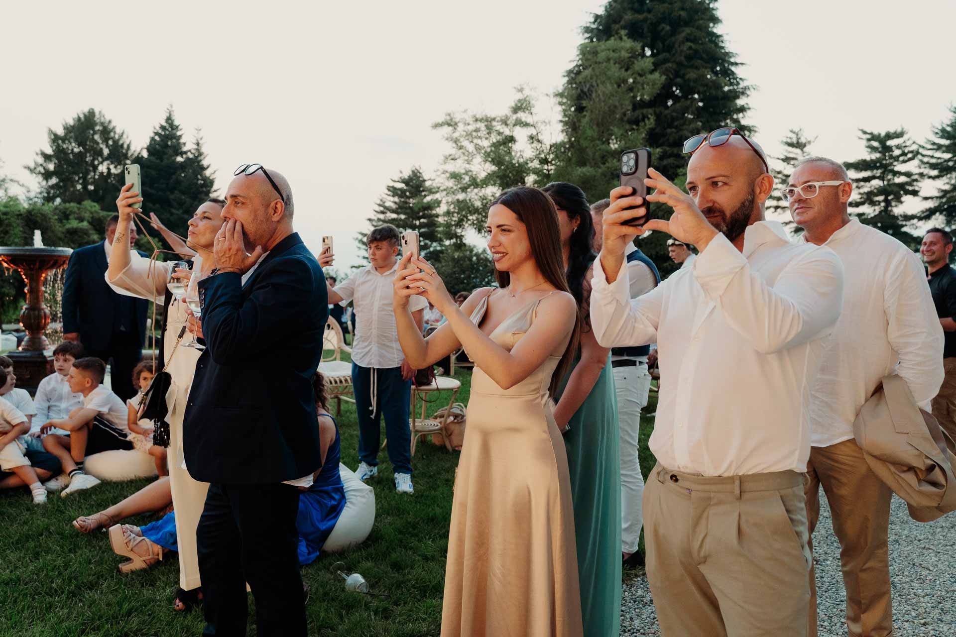 Gli invitati fotografano gli sposi con i telefoni, sul prato al tramonto