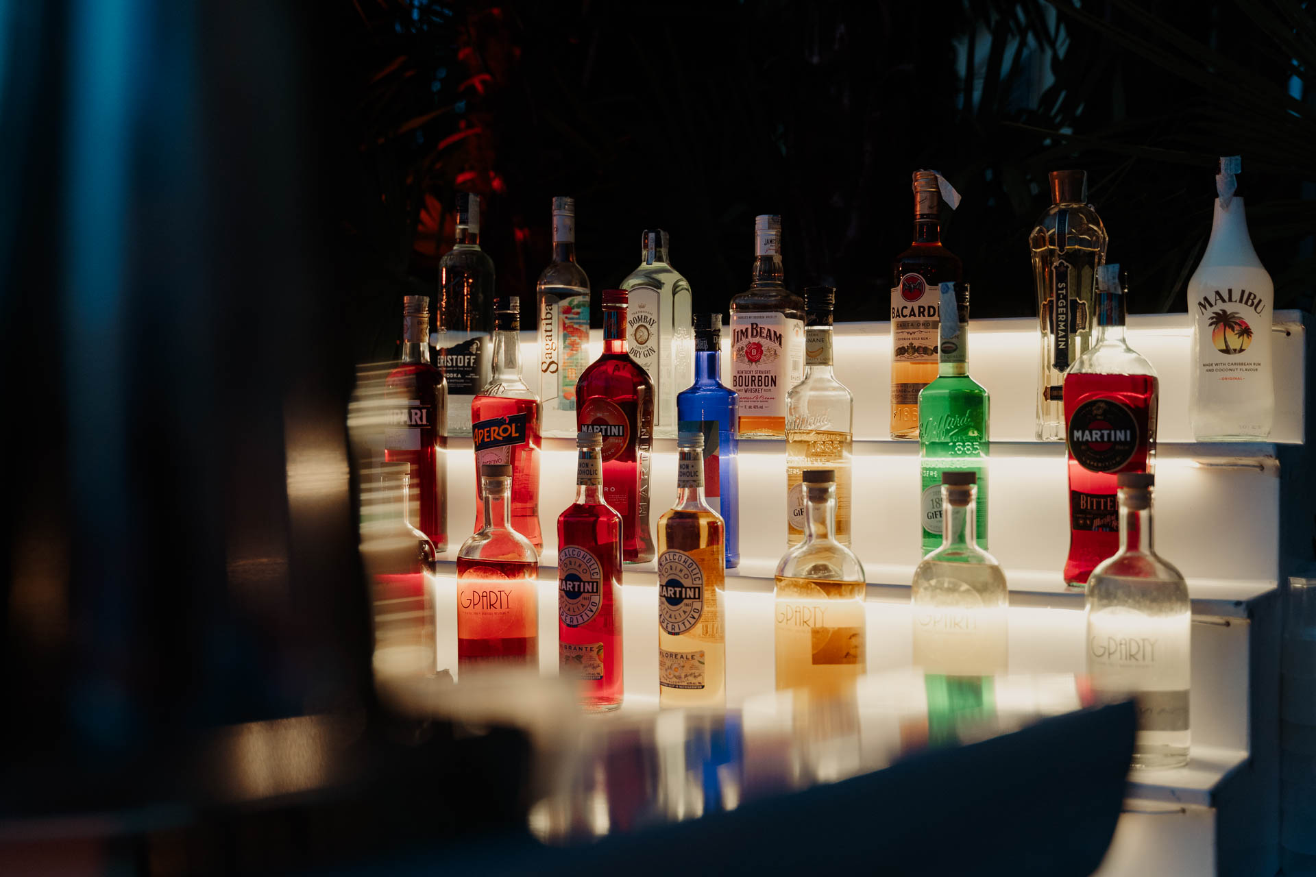 Il bancone del bar con le bottiglie illuminate, nel buio della sera