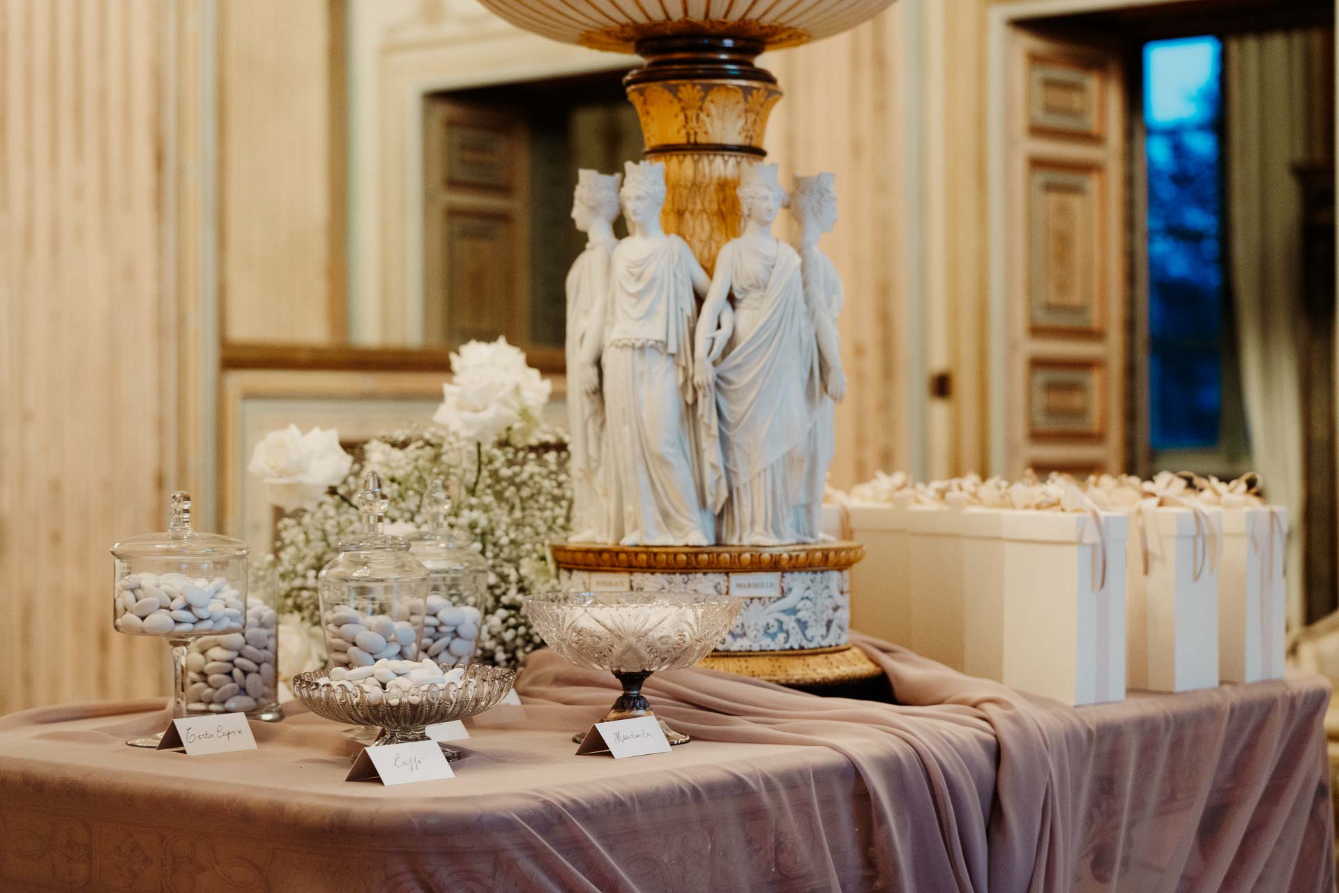 Il tavolo dei confetti e dei segnaposto sotto le statue della sala, con i sacchetti avorio