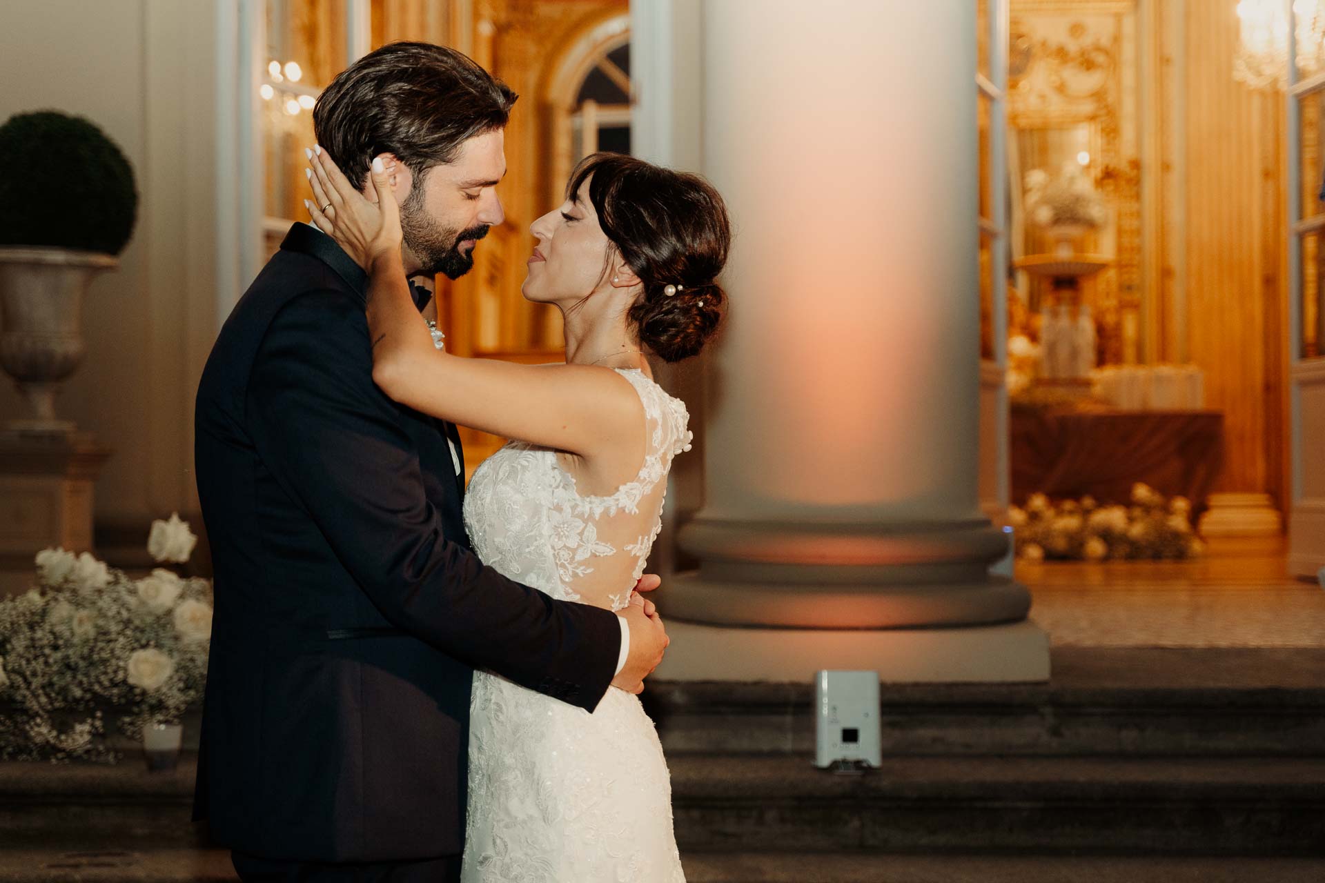Lo sposo stringe il viso della sposa e la guarda, accanto alla colonna illuminata